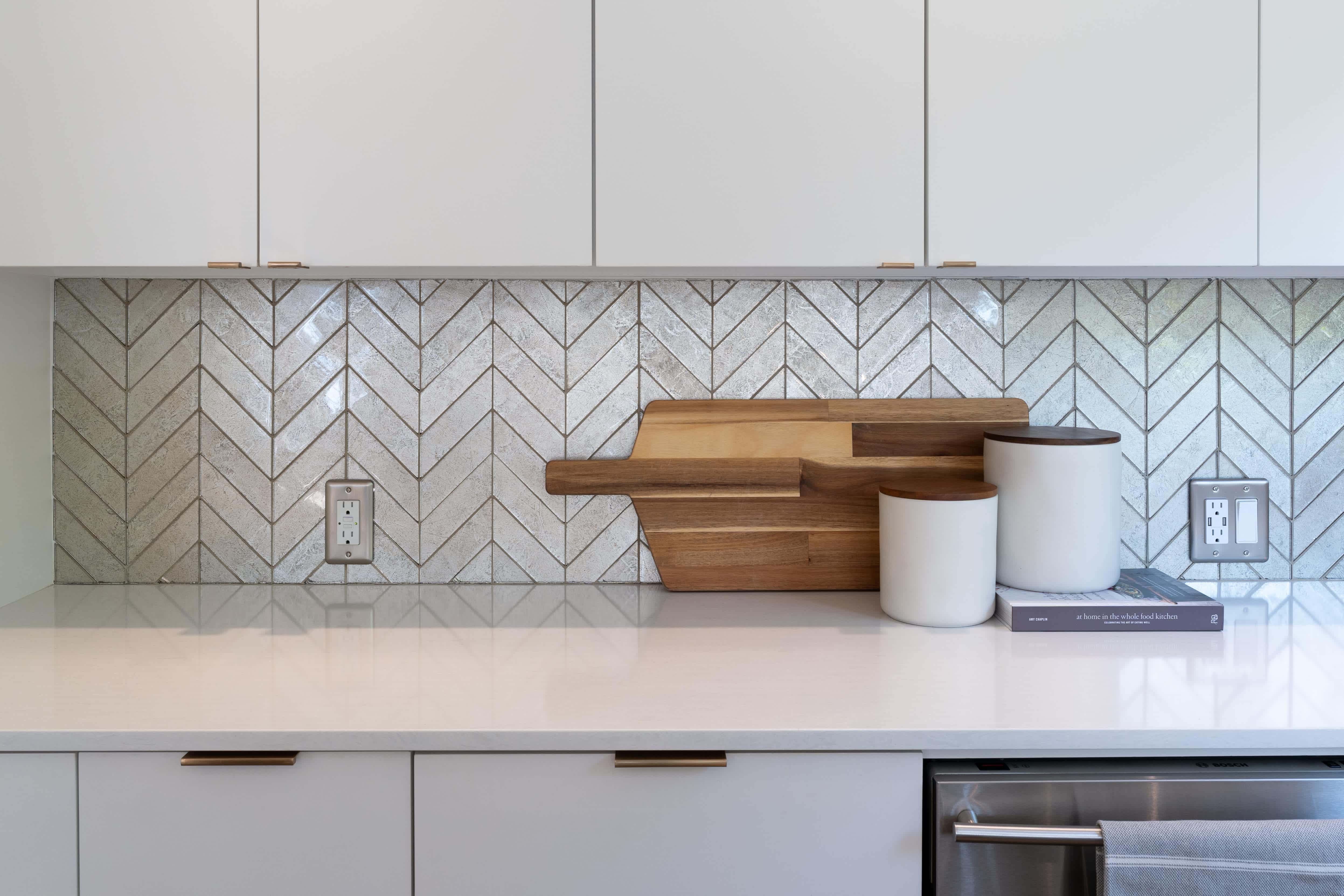 A white kitchen with a chevron backsplash made from iridescent tile