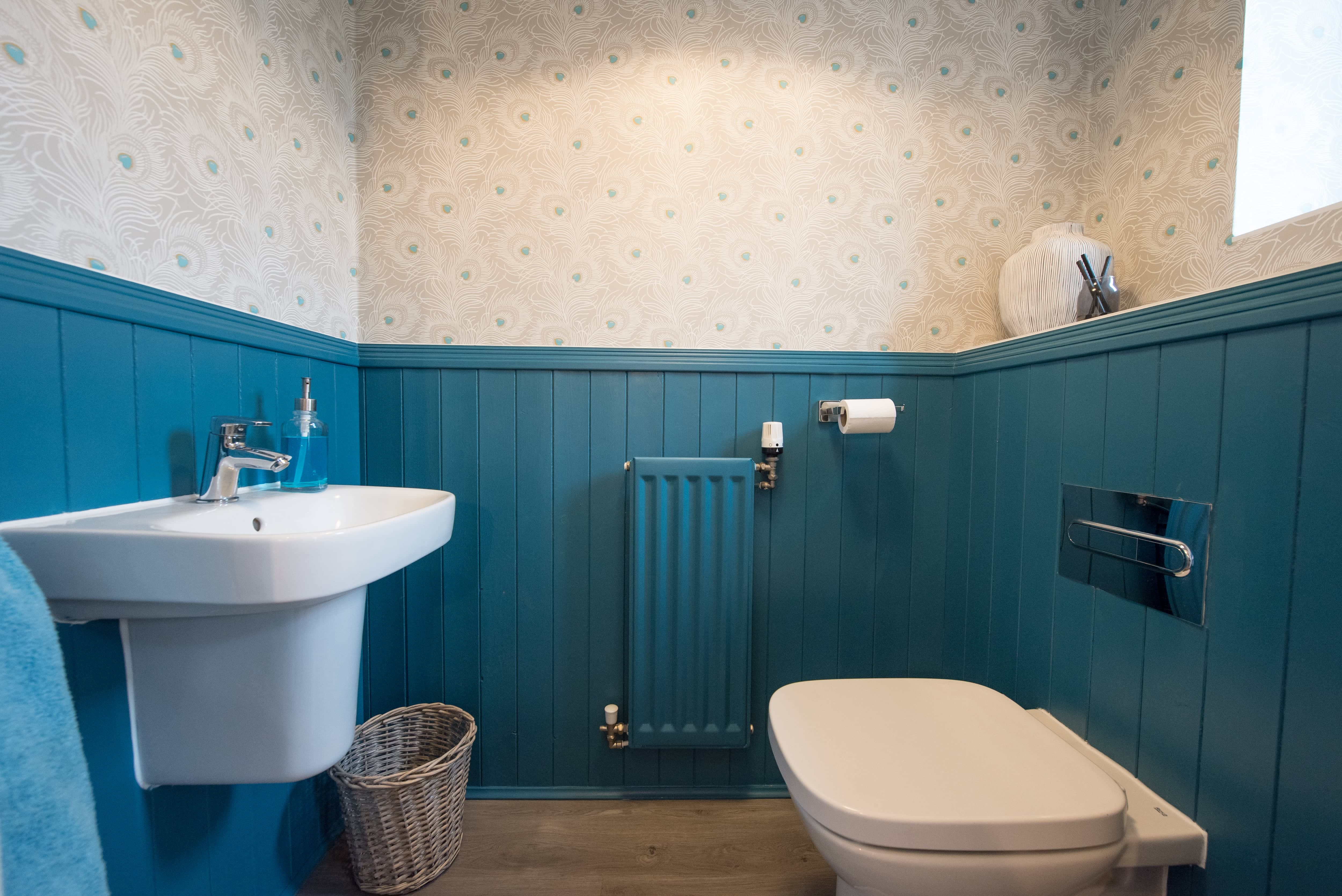 Small bathroom with blue wainscoting and blue-and-white peacock-inspired wallpaper