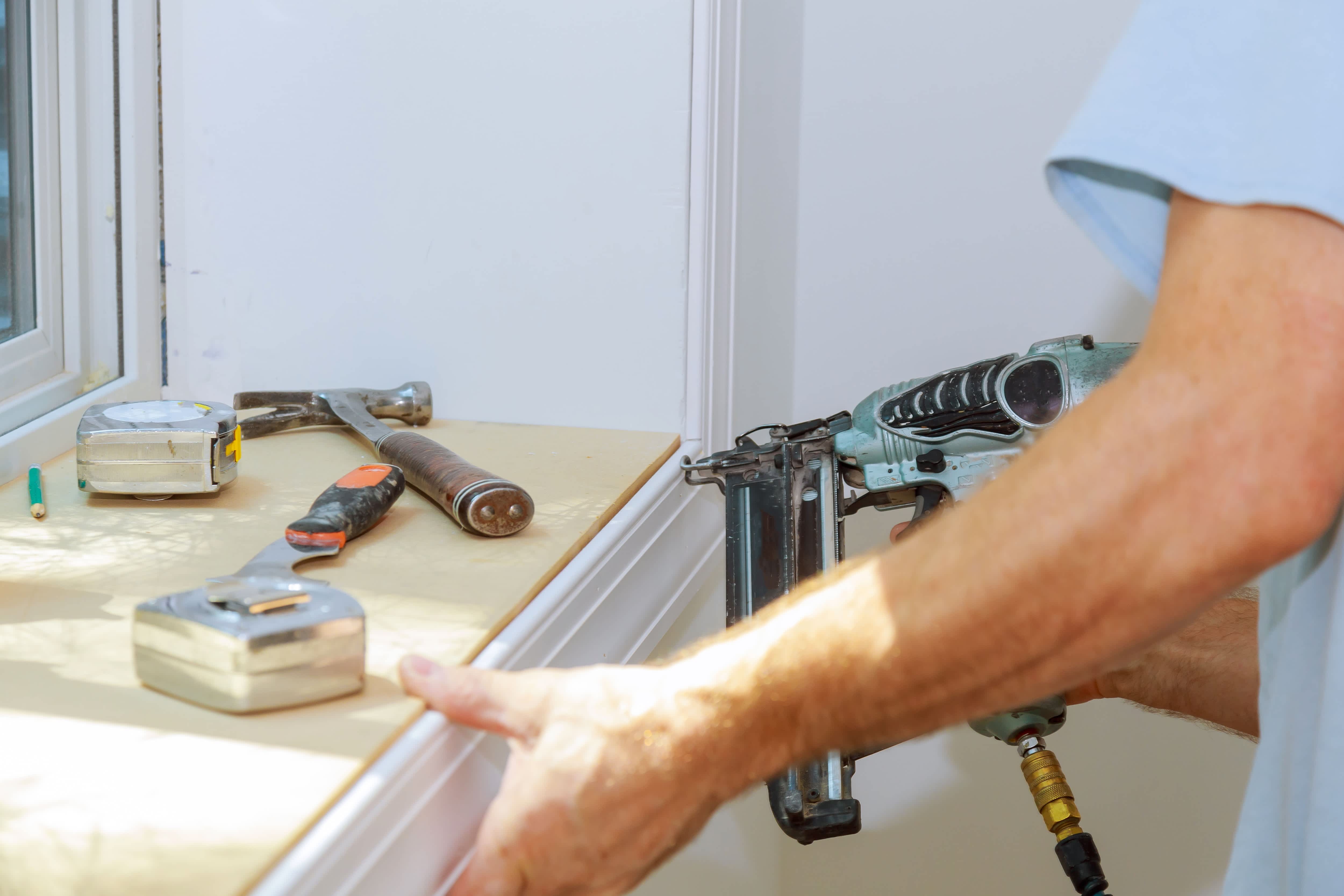 Carpenter using finish nailer to affix window moldings