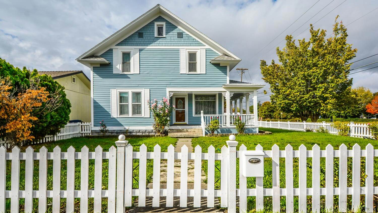 The exterior of a blue and white craftsman house with a white picket fence