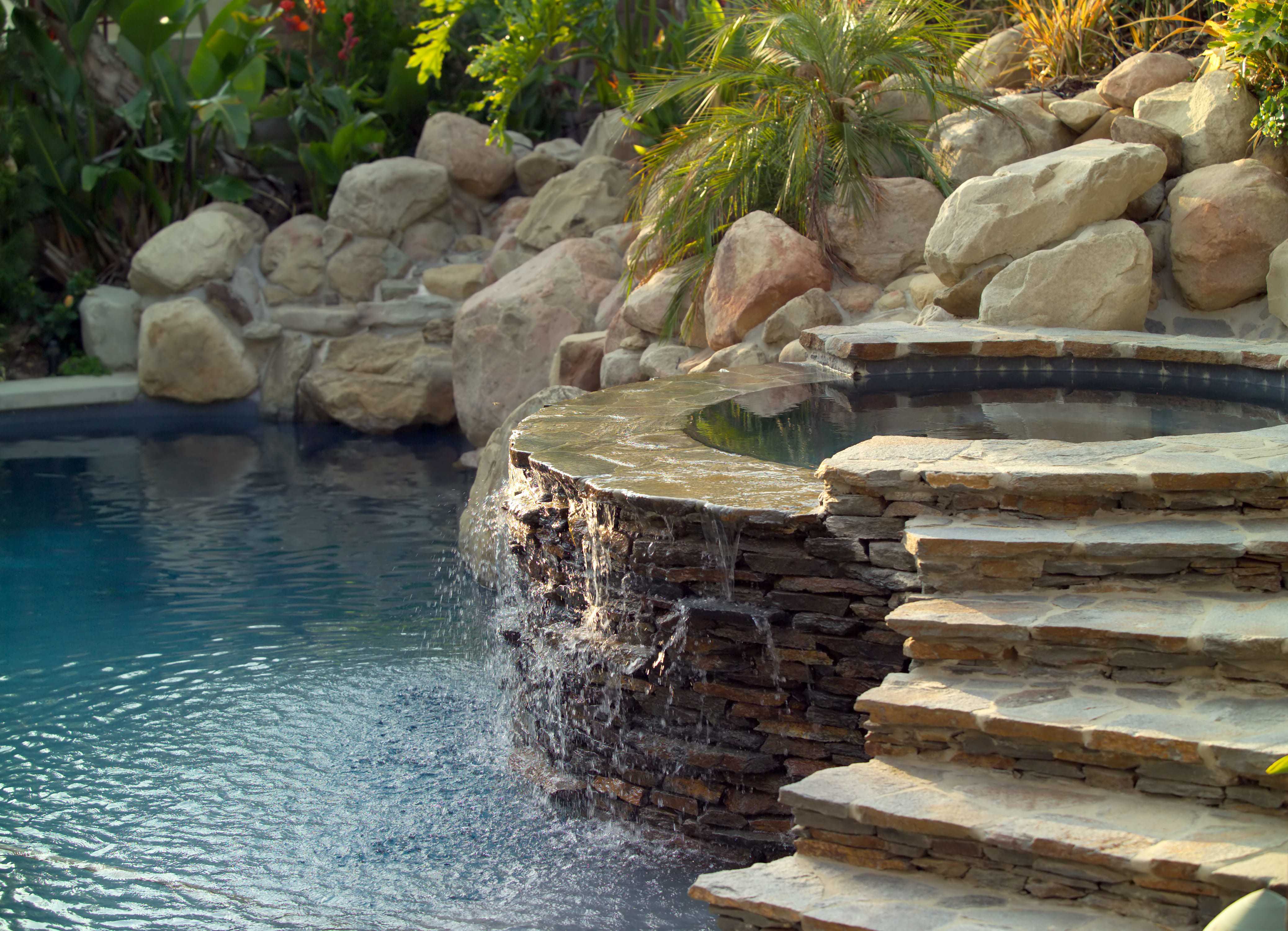 A hot tub attached to a pool with stone steps leading into it