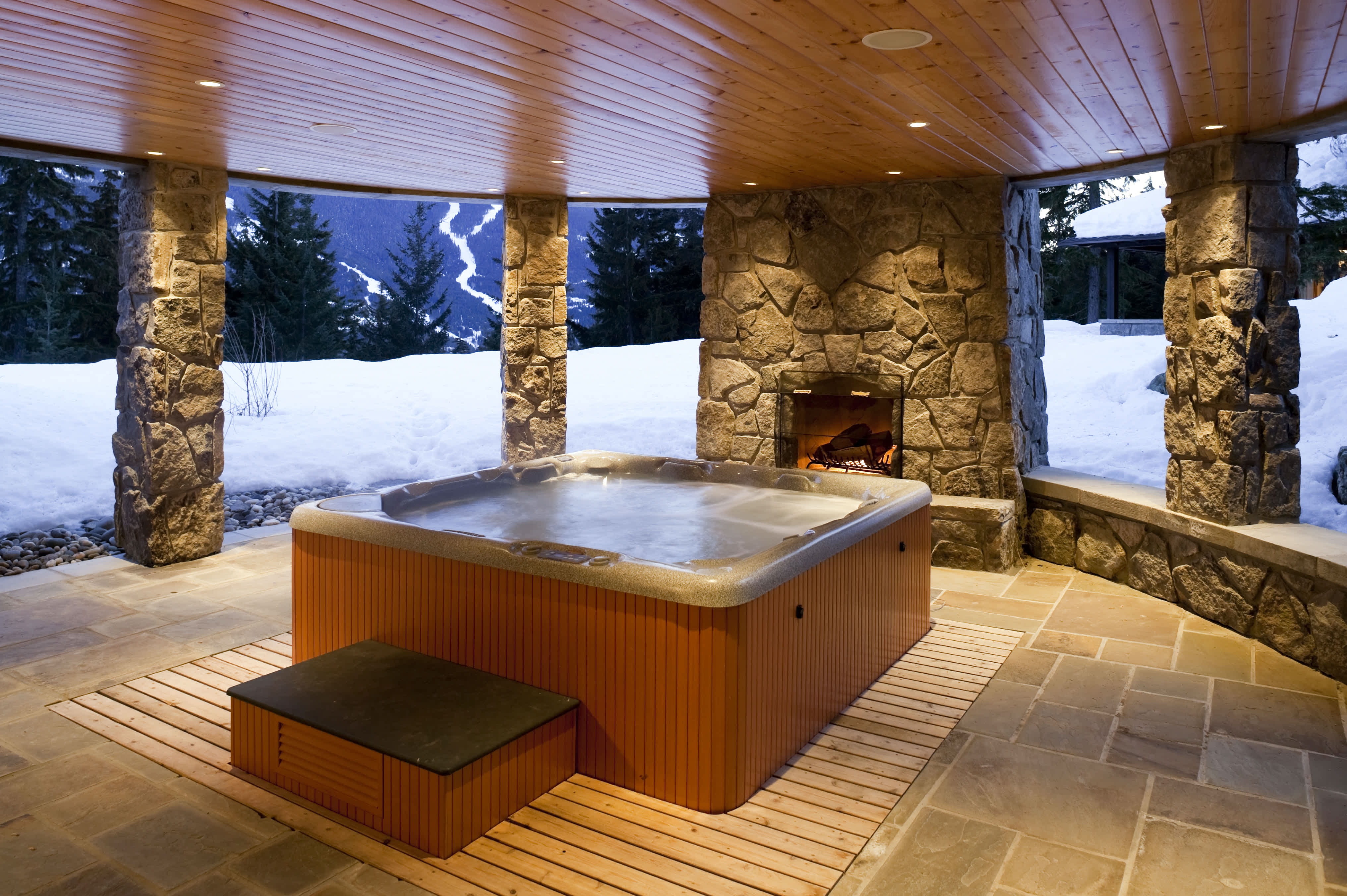 A covered patio with a hot tub surrounded by a stone floor patio