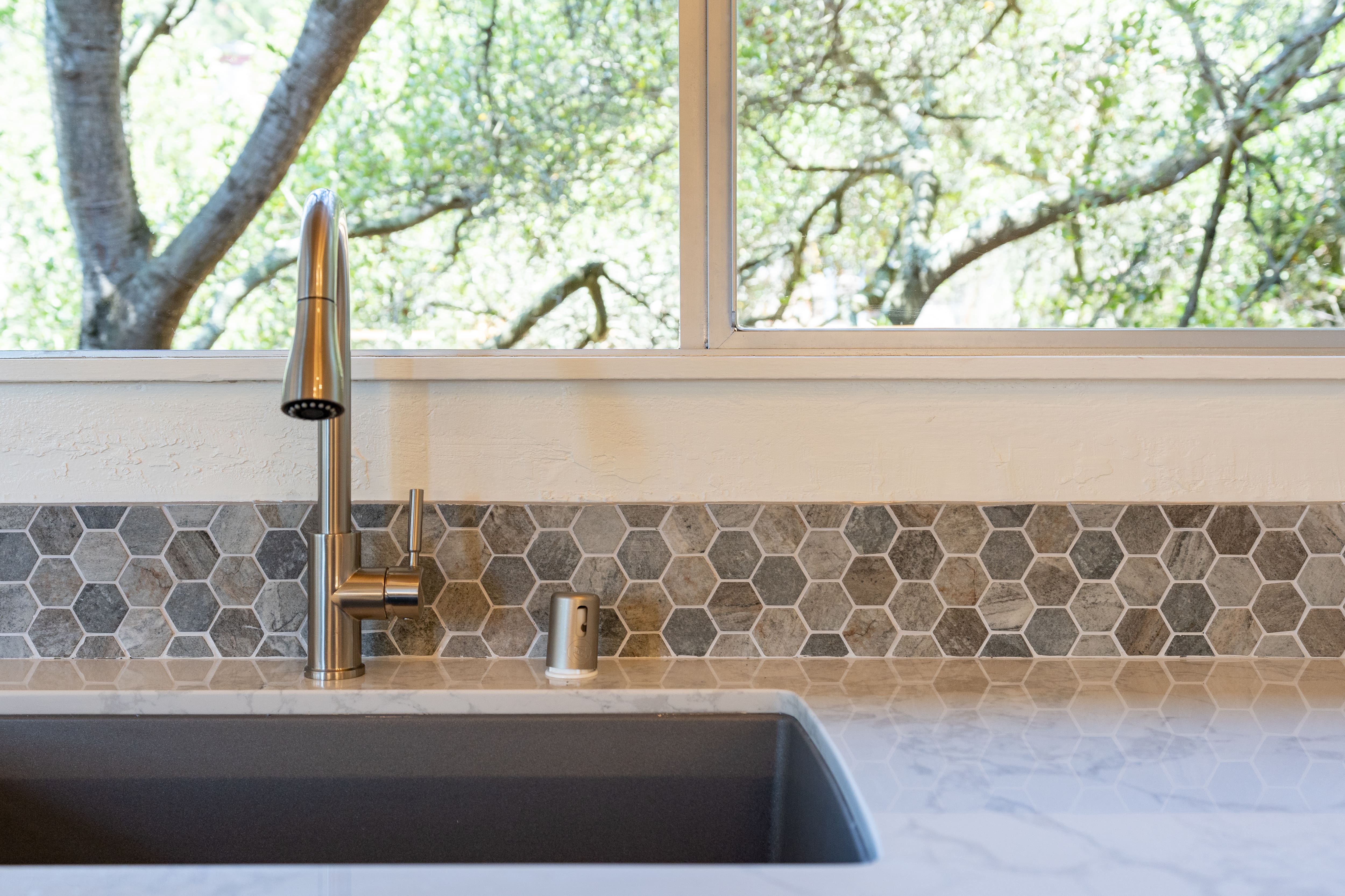 A metal sink with multi-colored backsplash made of hexagon tiles