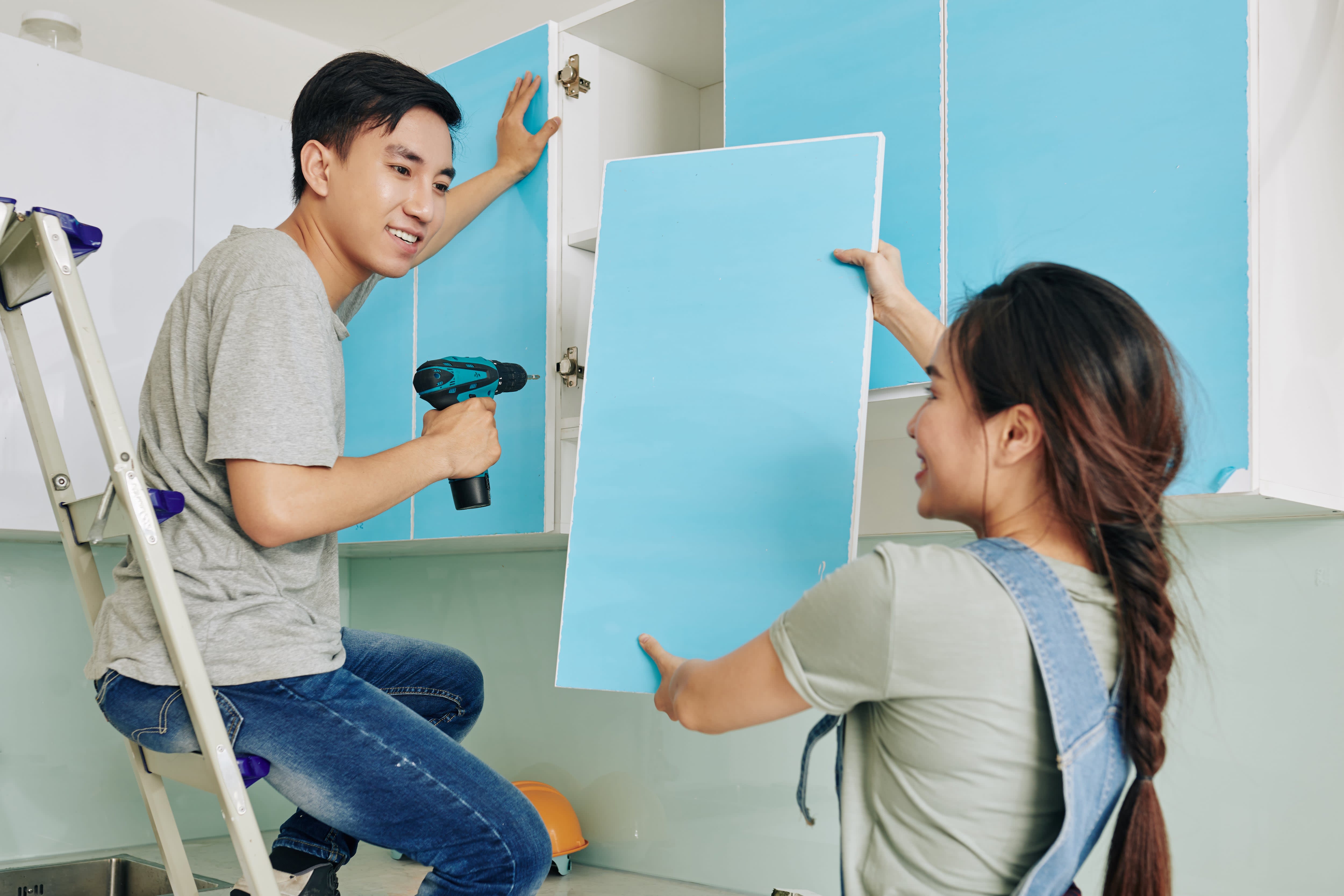 A couple in a kitchen doing a DIY project on light blue cabinets