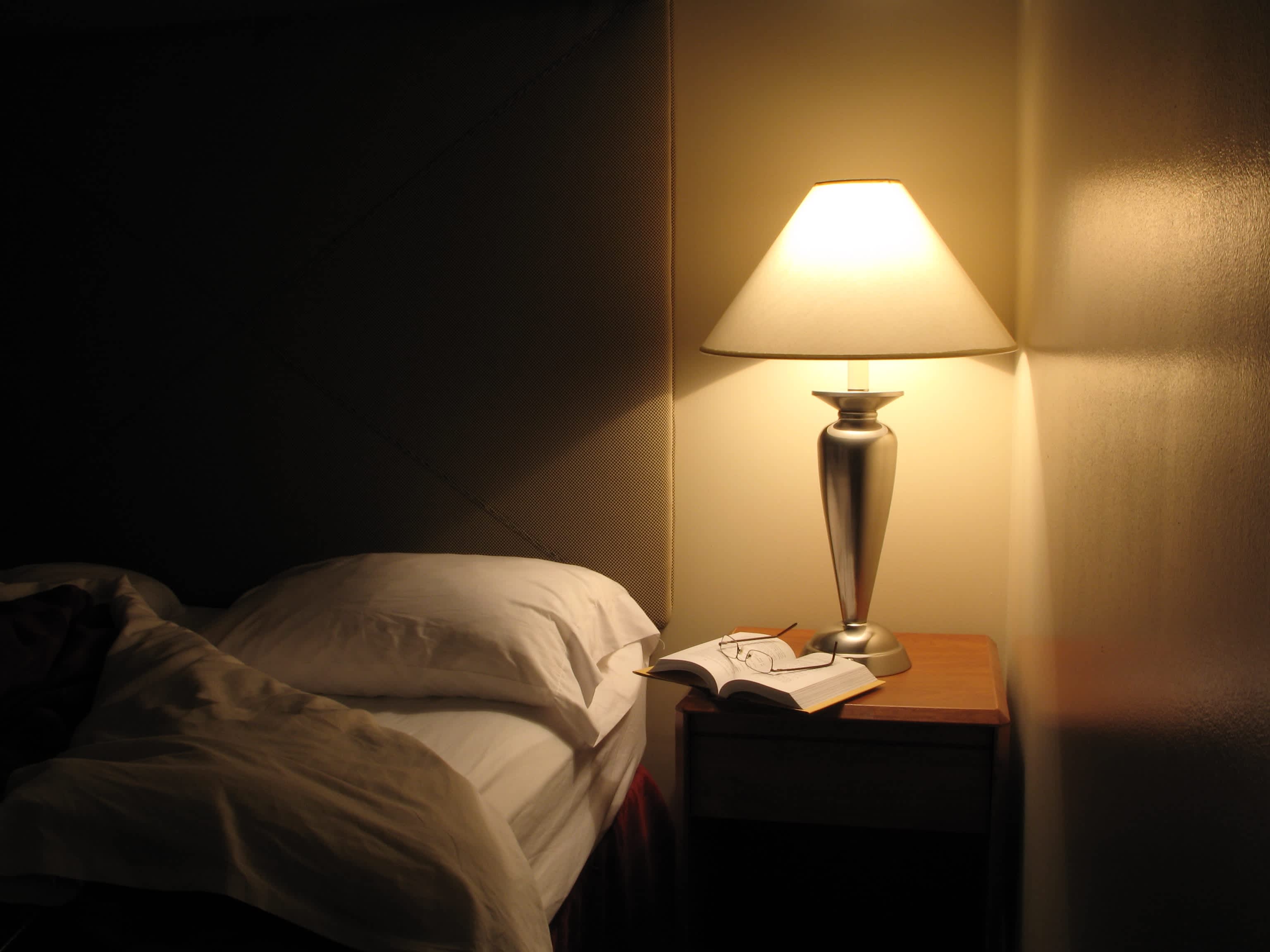 A corner shot of a bedroom lit with a nightside table lamp