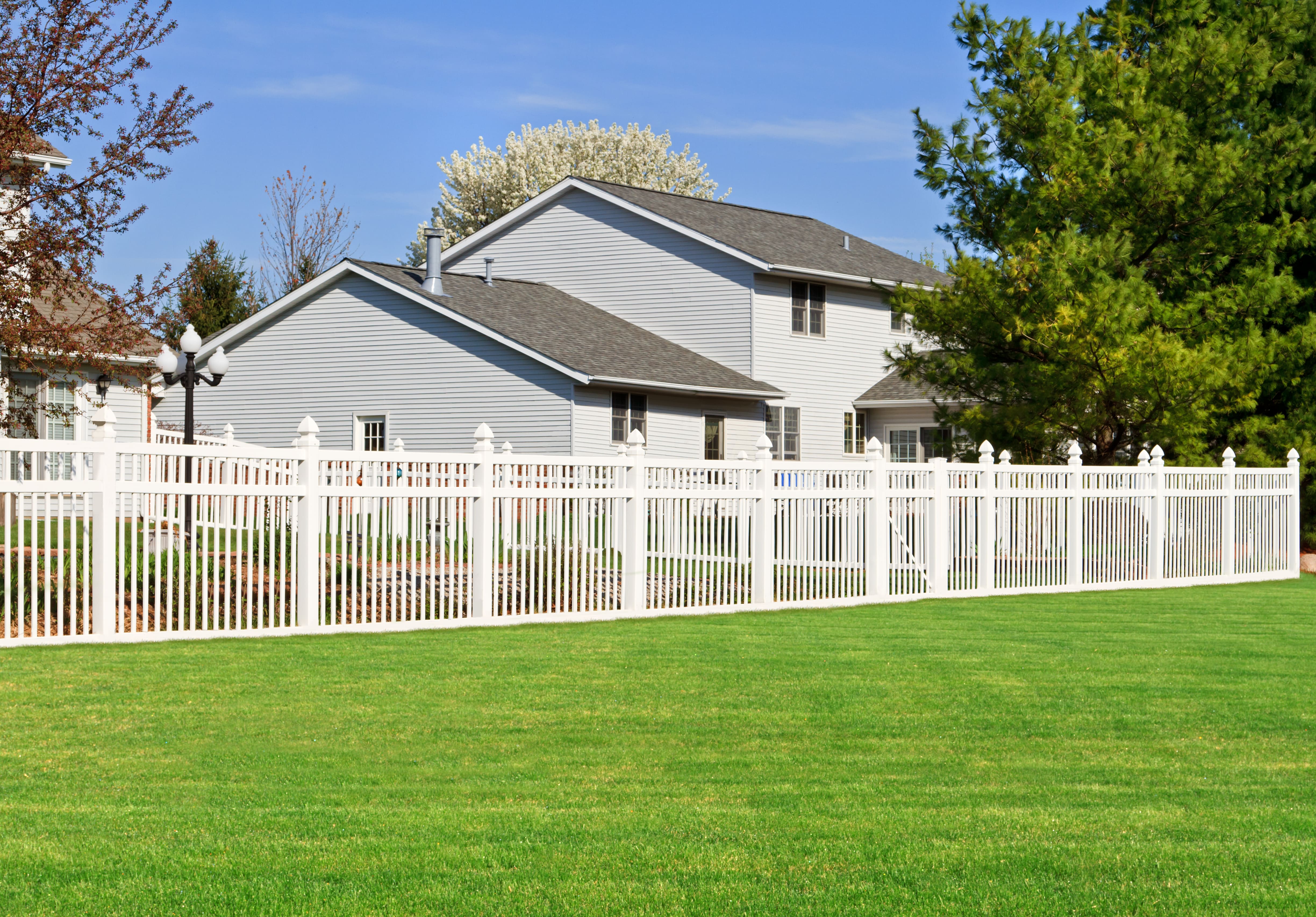 A gray home with a white vinyl fence in front of it