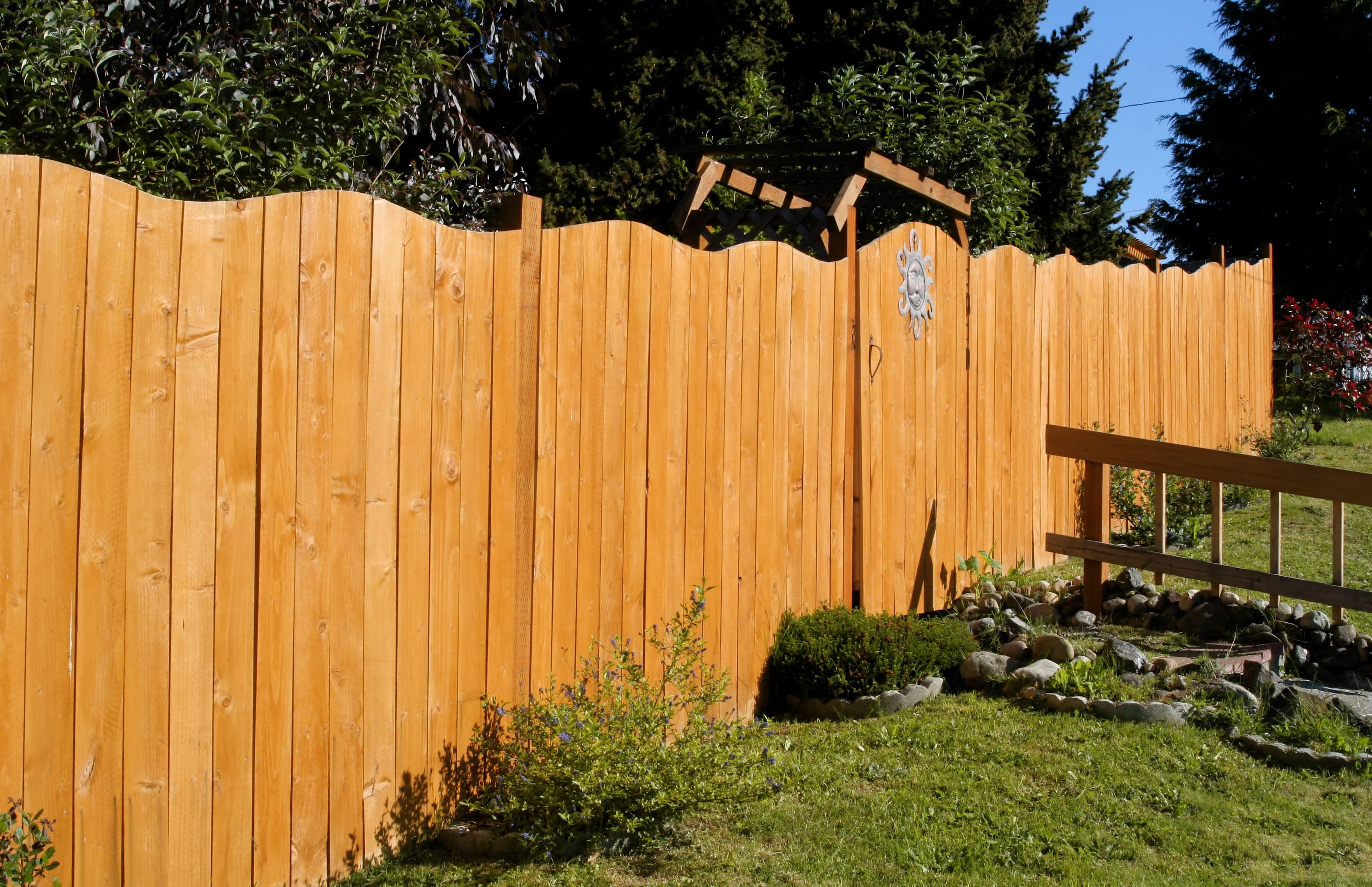 A tall fence with a curved, wavy top in the sunlight