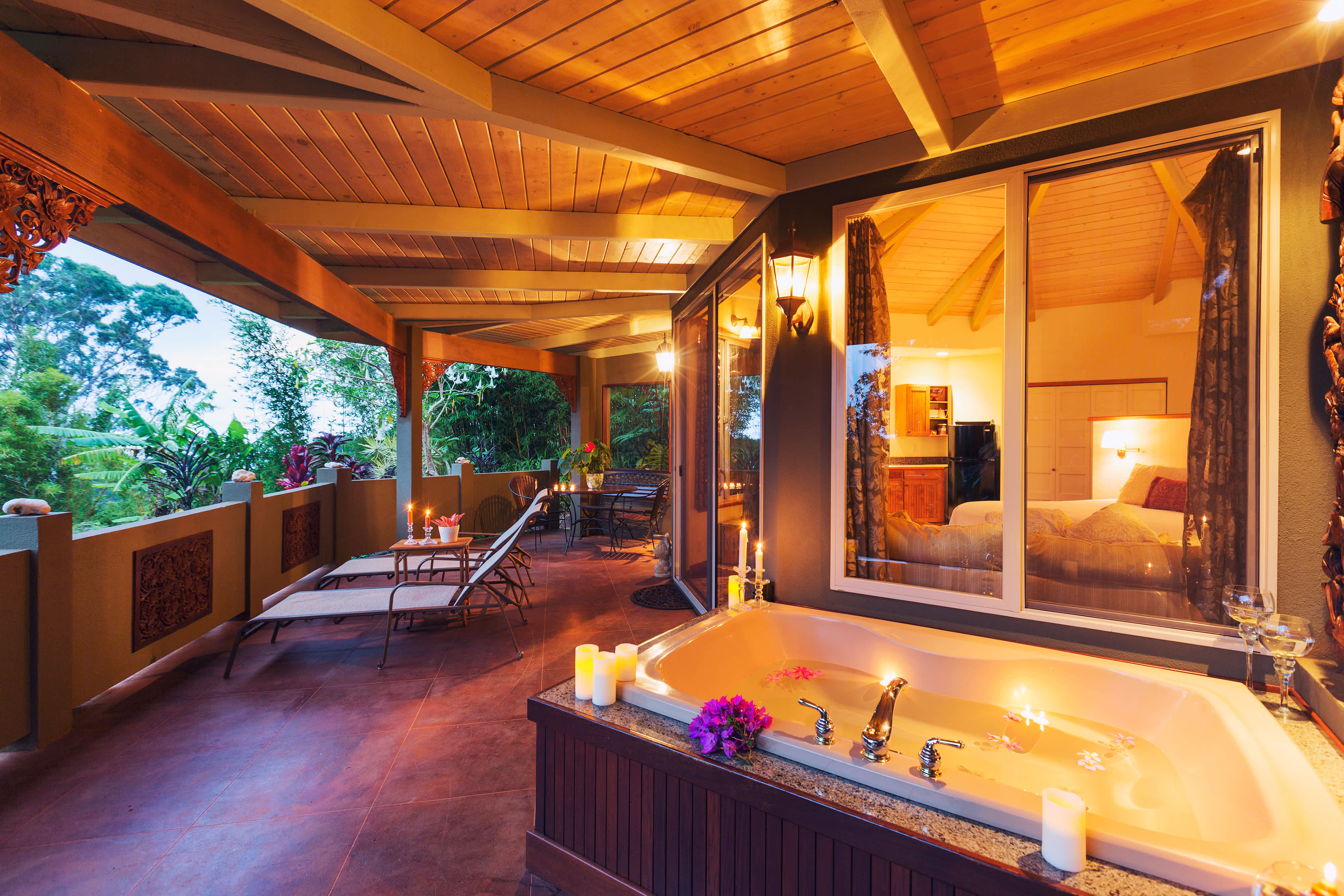 A warmly lit covered deck with a hot tub positioned near the windows