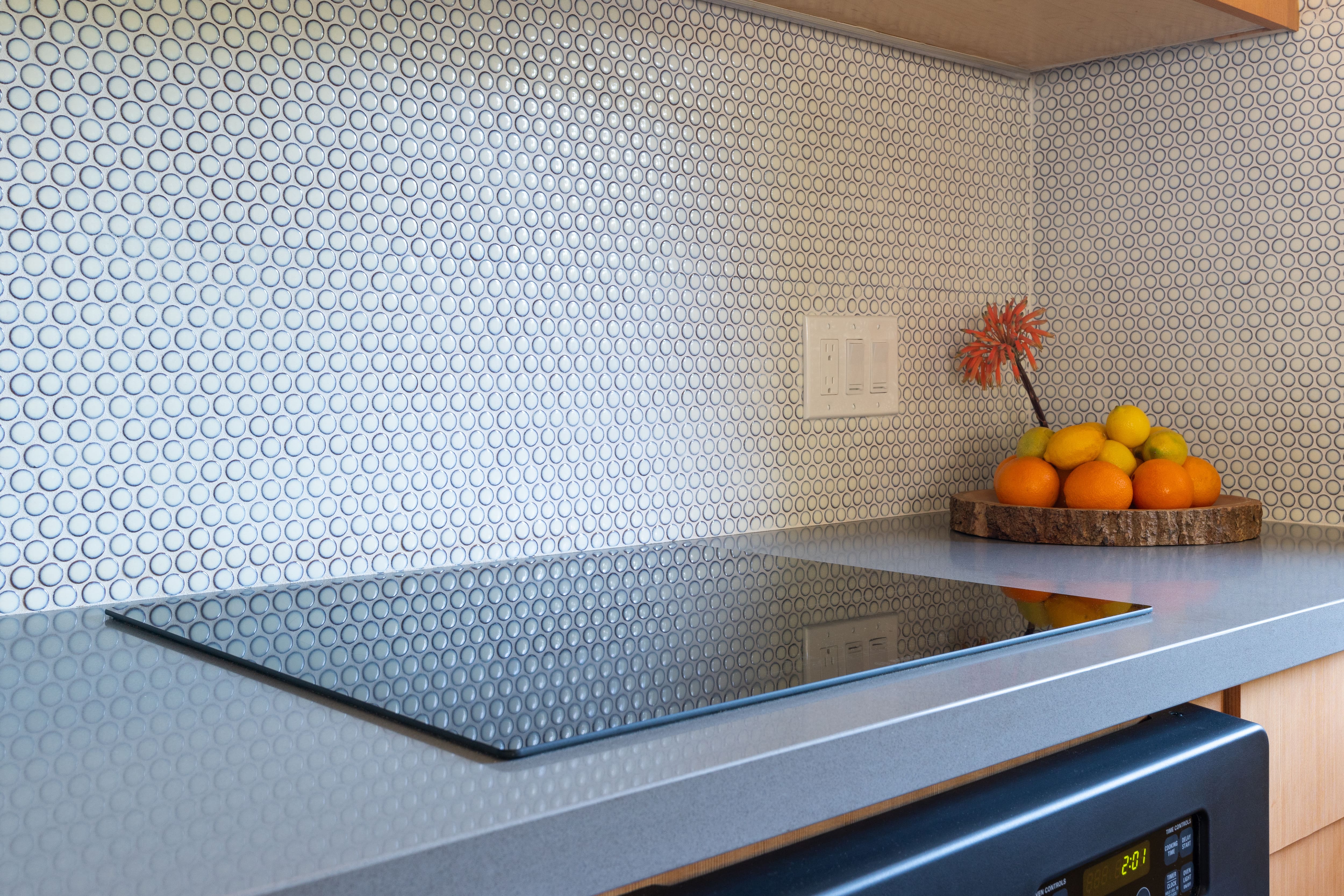 A gray penny tile backsplash above a flat top stove in a modern kitchen