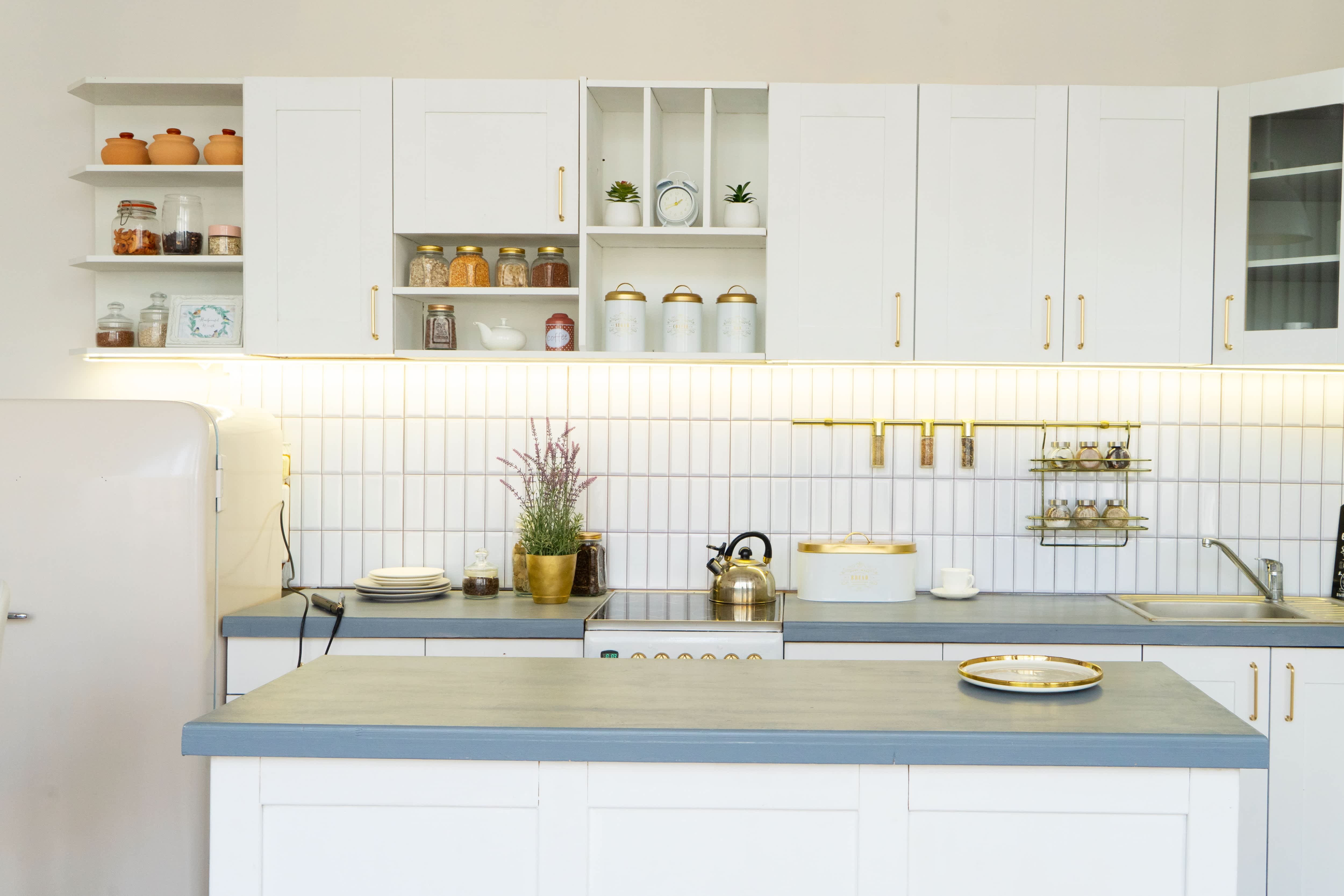 A white kitchen with gold accents and vertically stacked tile