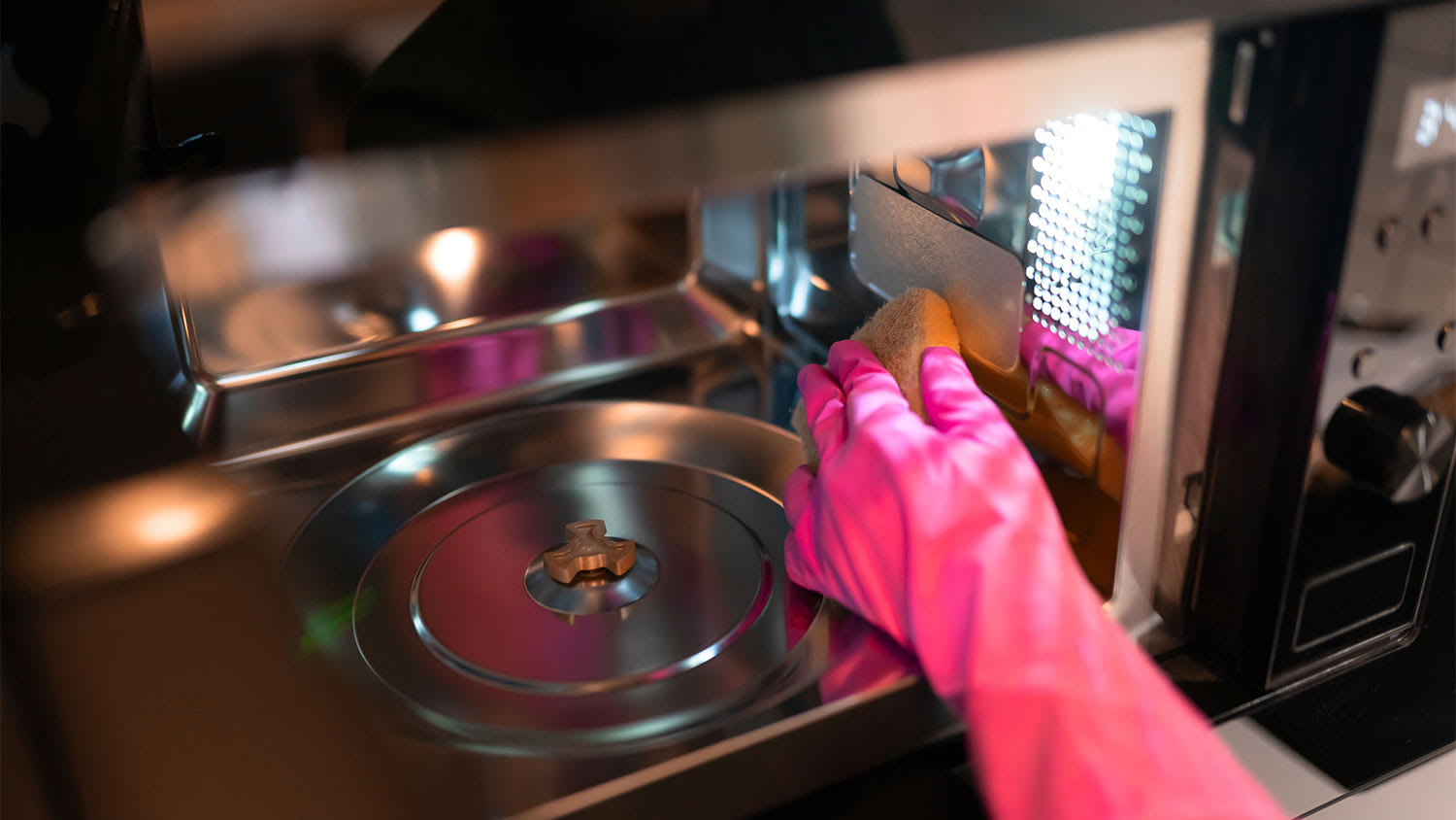 A hand cleans a microwave with a sponge