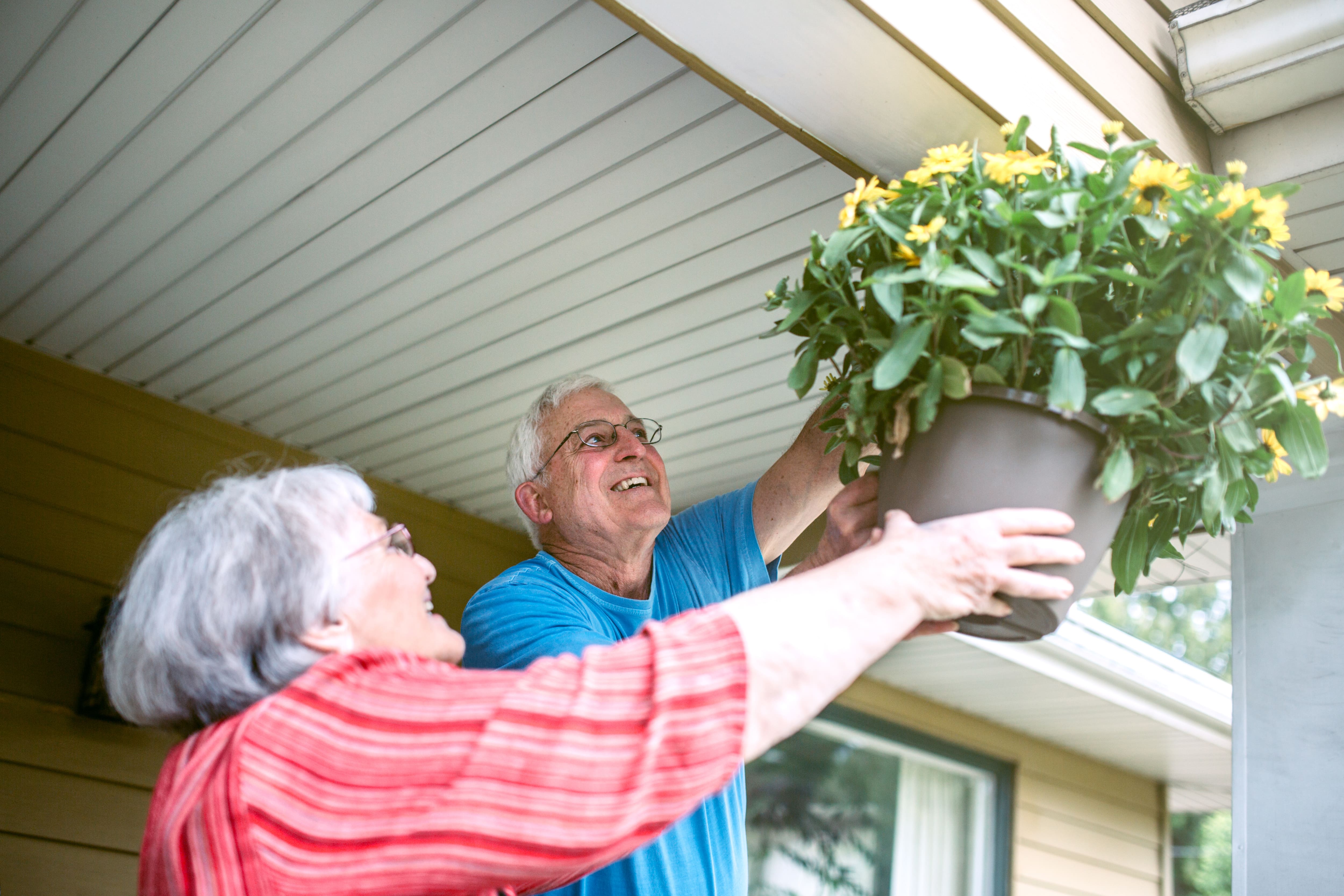 Senior couple hanging flower basket from covered front porch