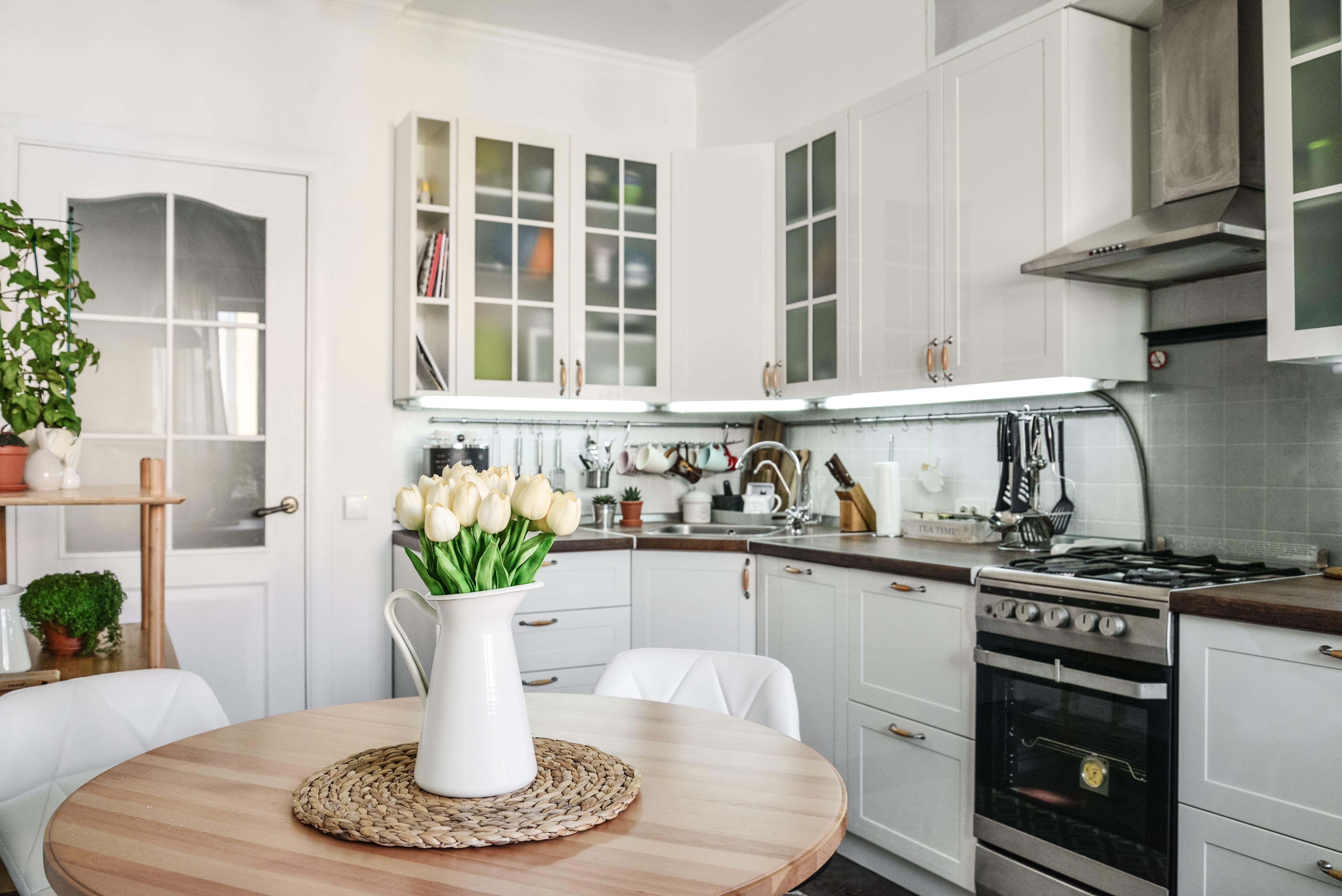 A small kitchen with white walls, cabinets, and a bouquet of white tulips
