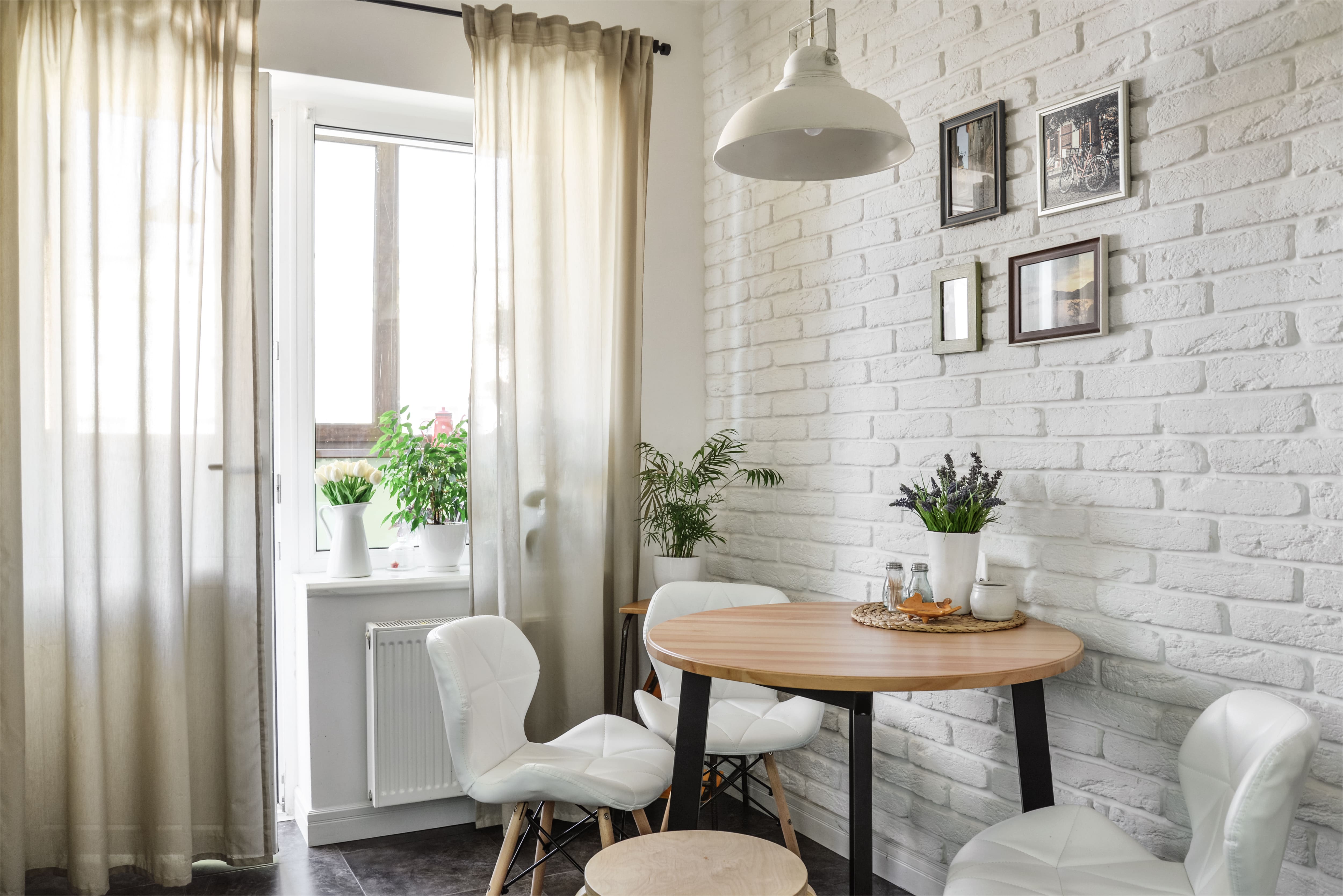 A kitchen with natural light, white curtains, and a round dining table