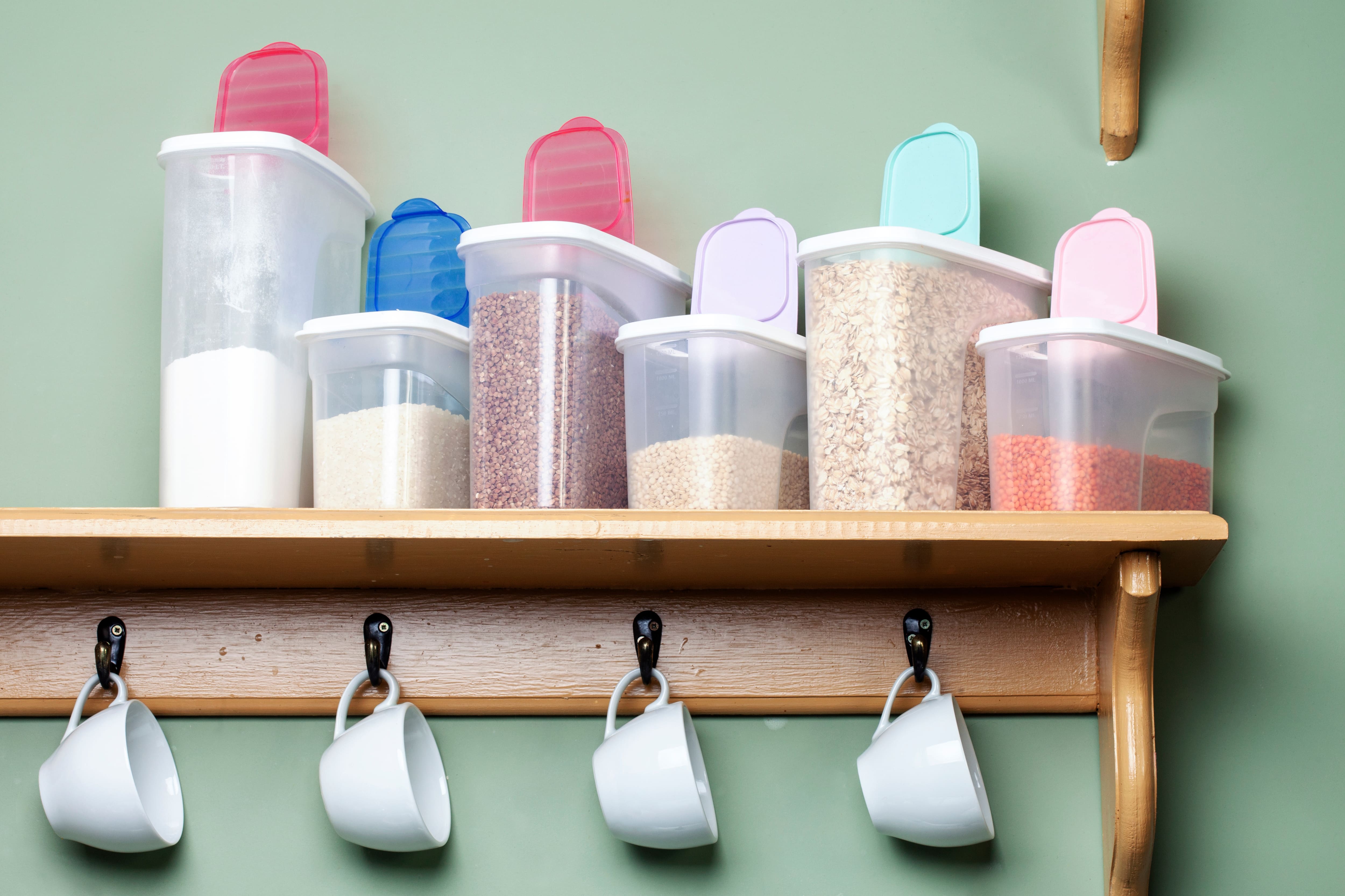 A floating shelf with clear containers filled with colorful grains and hanging coffee mugs