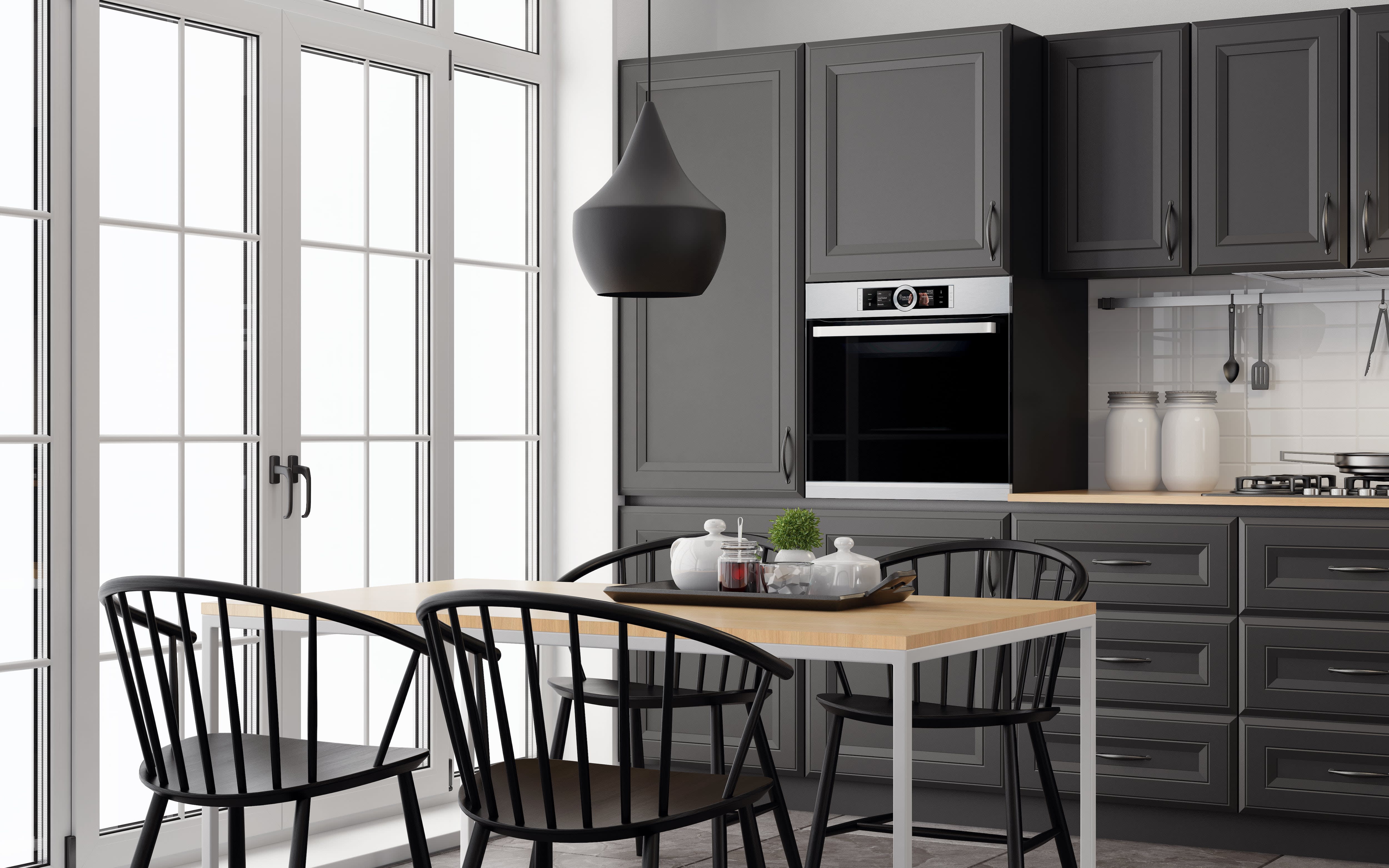 A black and white kitchen with tall cabinets, a table, chairs, and large windows