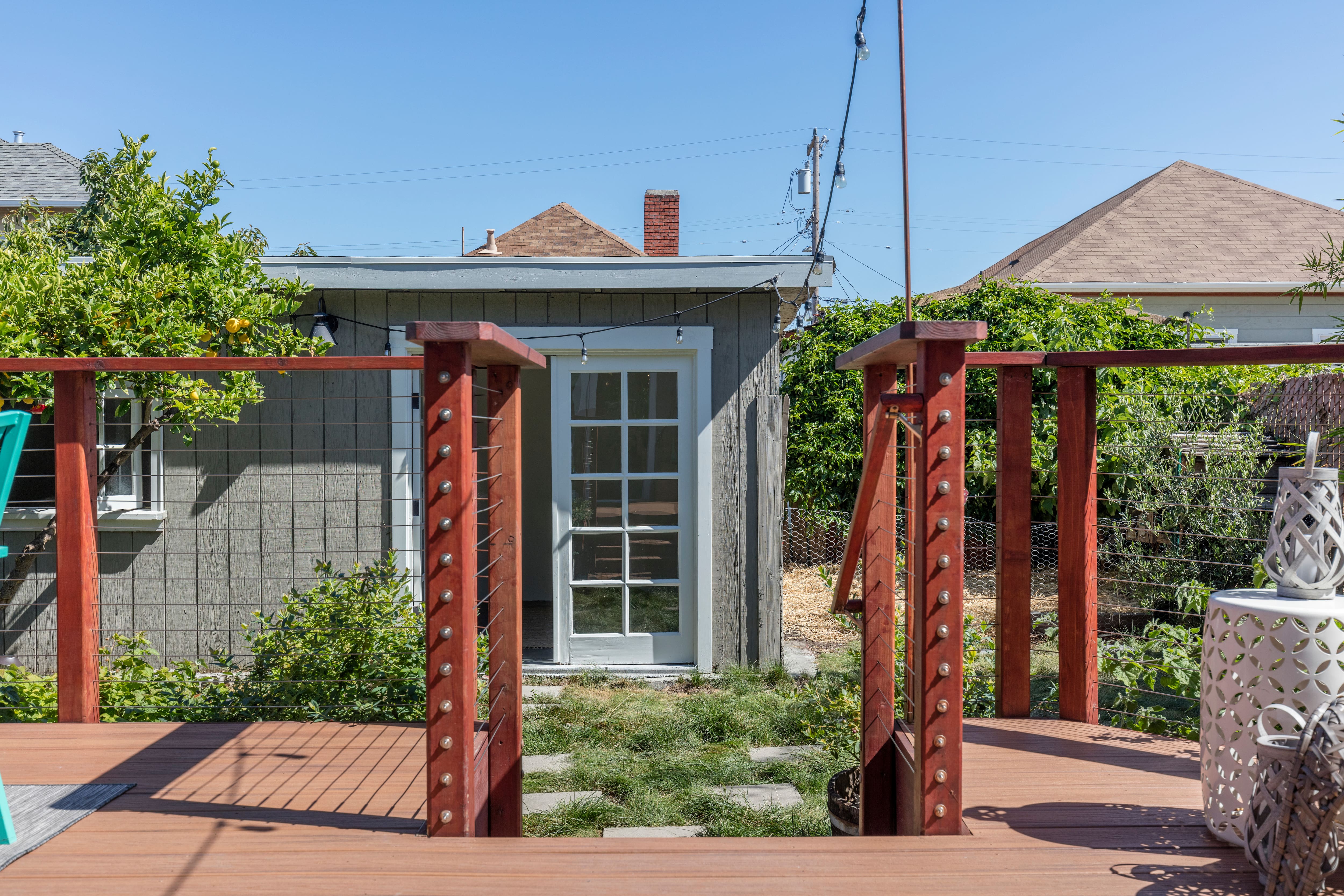 Wooden deck with steel mesh railing overlooking a backyard and guest house