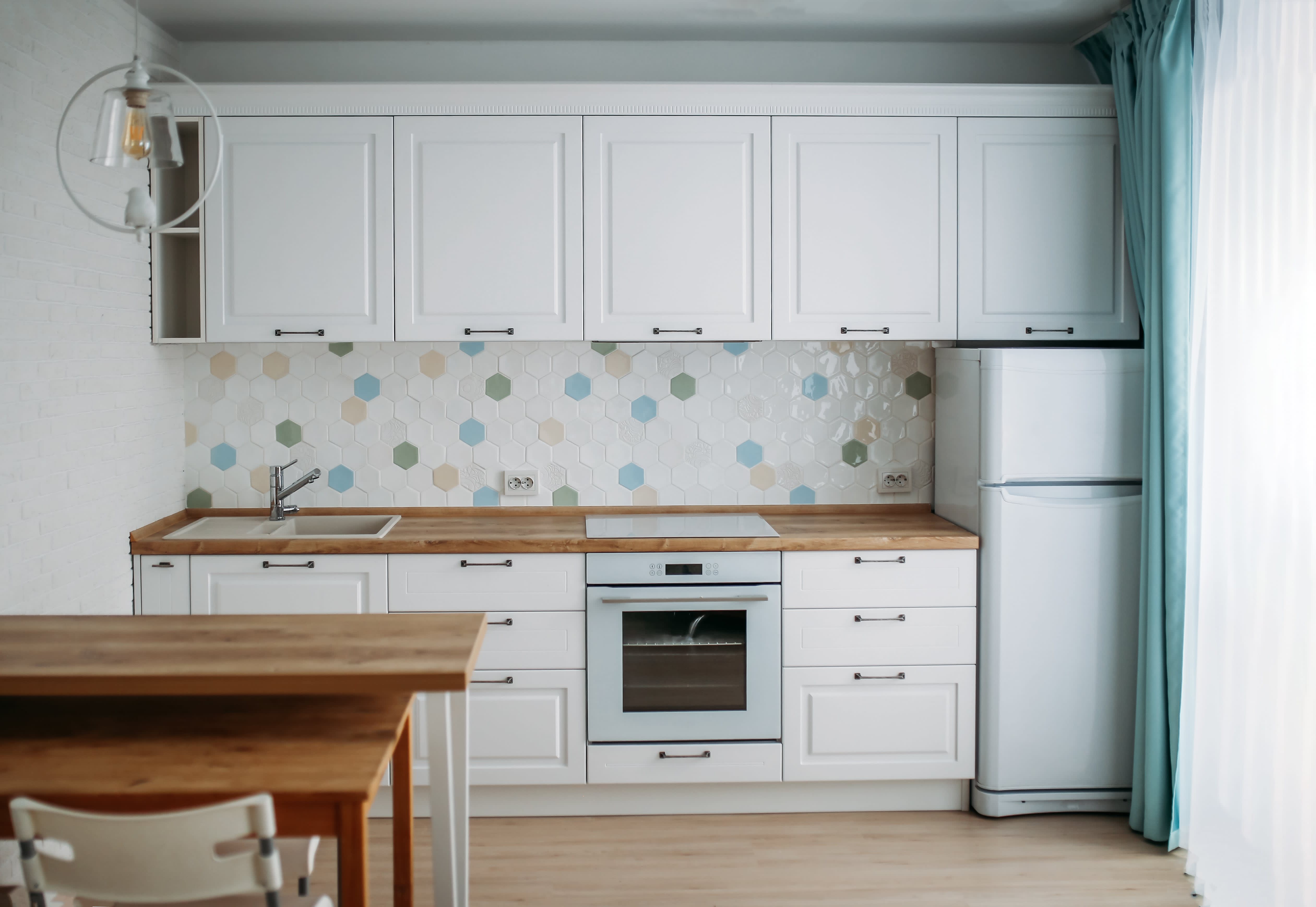 A small white kitchen with clean countertops and a small, clean wooden table