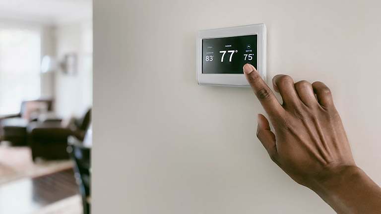 A hand adjusts the temperature of the room using a thermostat