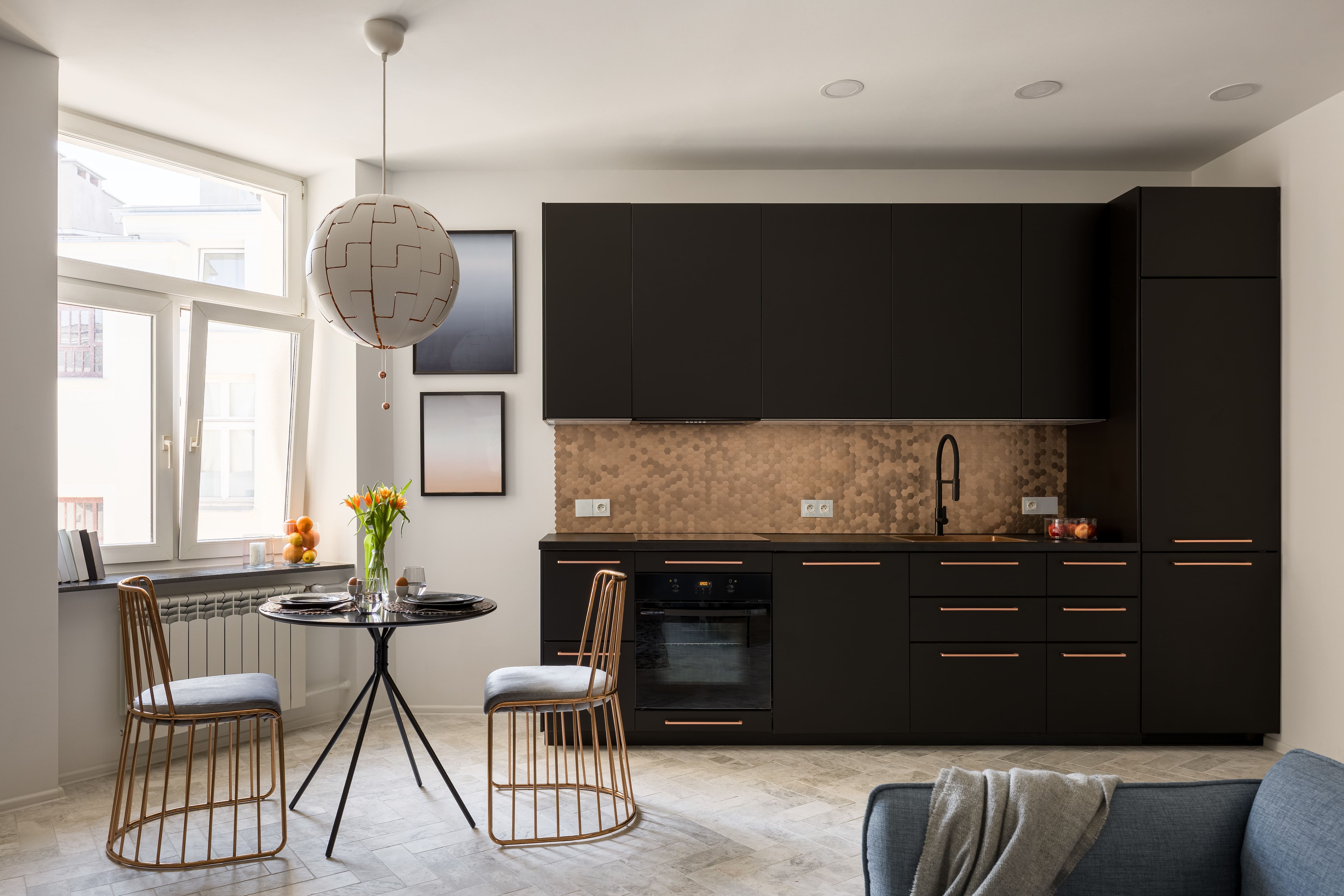 A black kitchen with gold backsplash, chairs, and hanging light