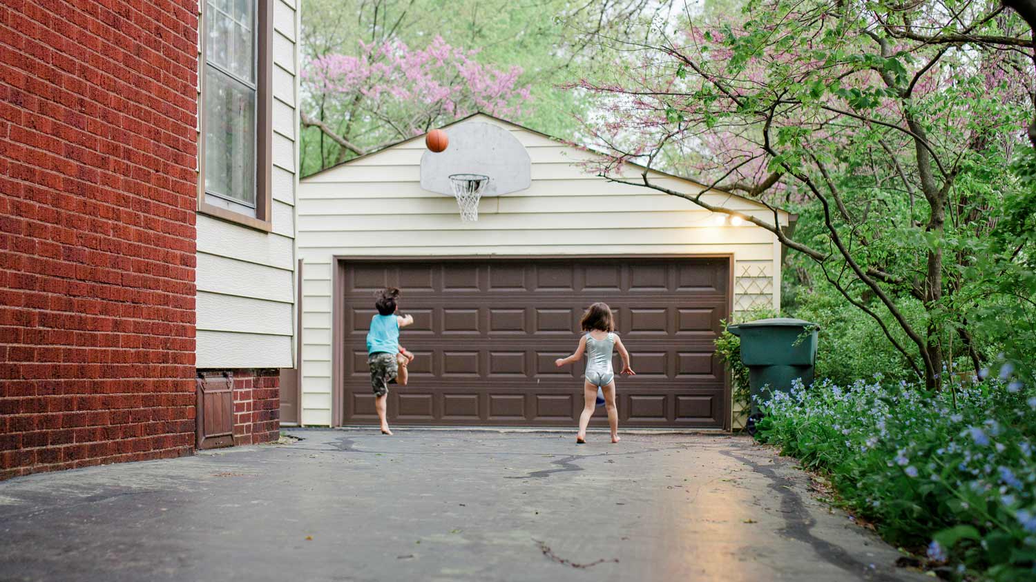 A boy shoots a basketball in front of home’s garage