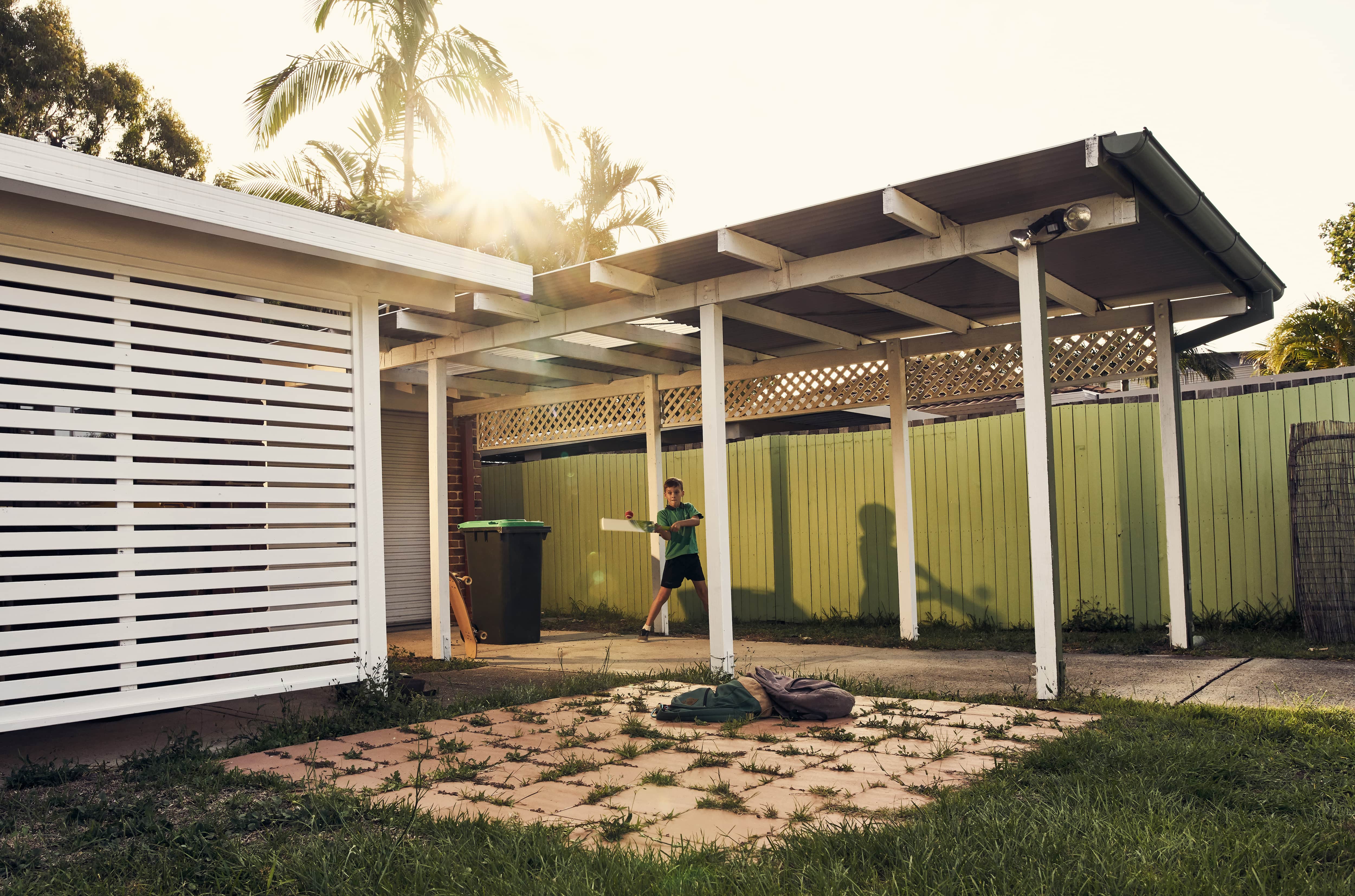 Boy hitting a ball in backyard under carport
