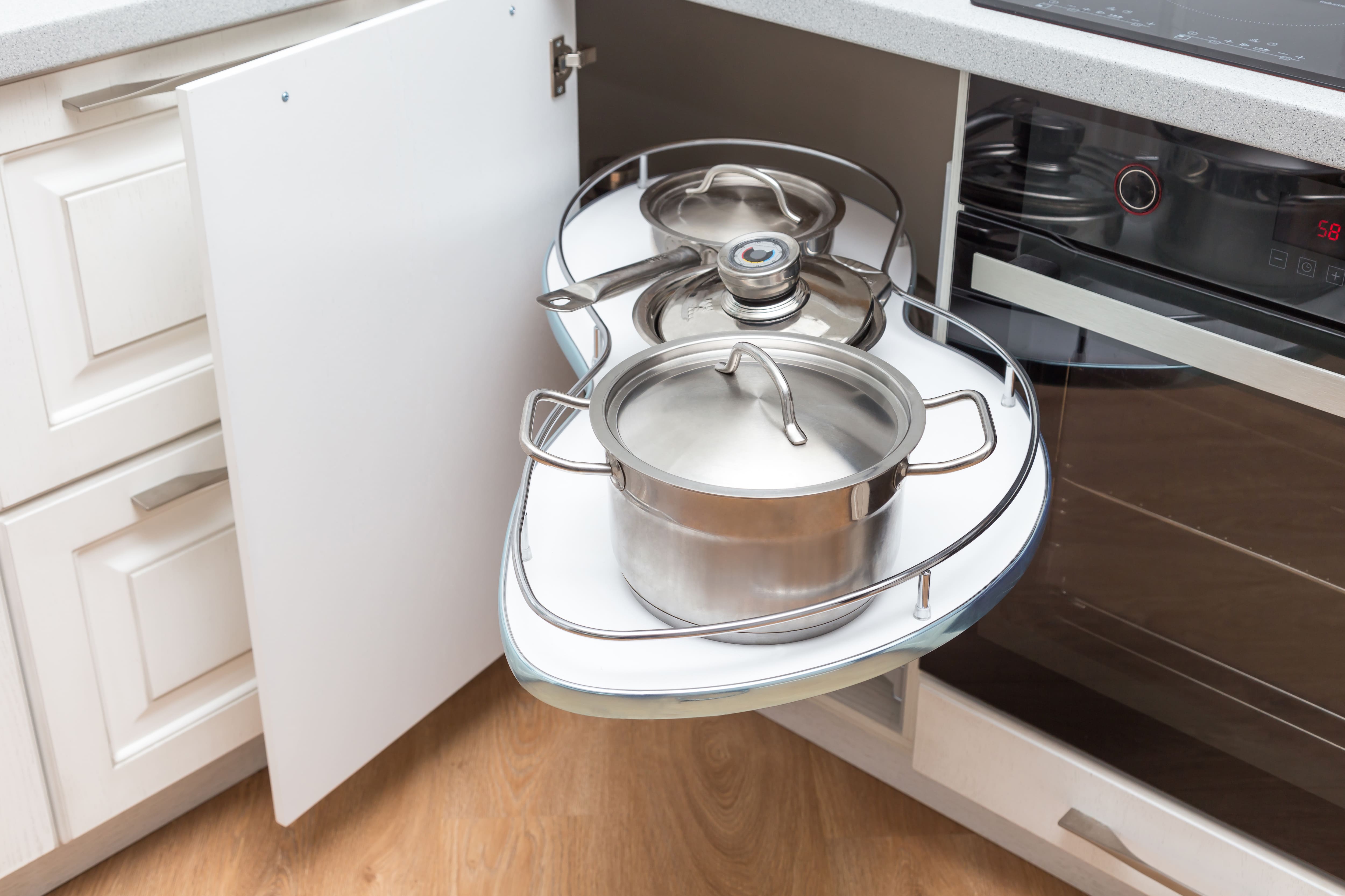 A corner kitchen cabinet with pull out shelves displaying cookware