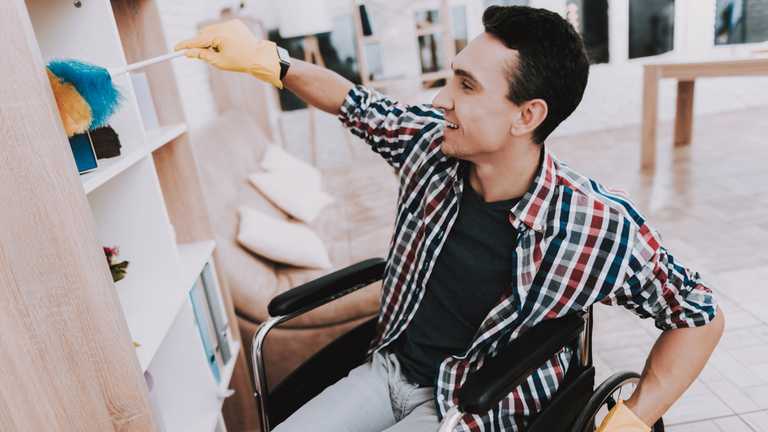 Young man in wheelchair cleaning bookcase