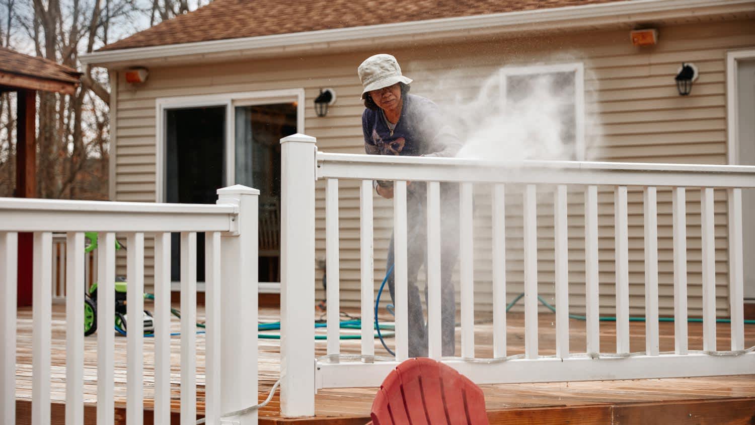 A woman pressure washing a house’s porch