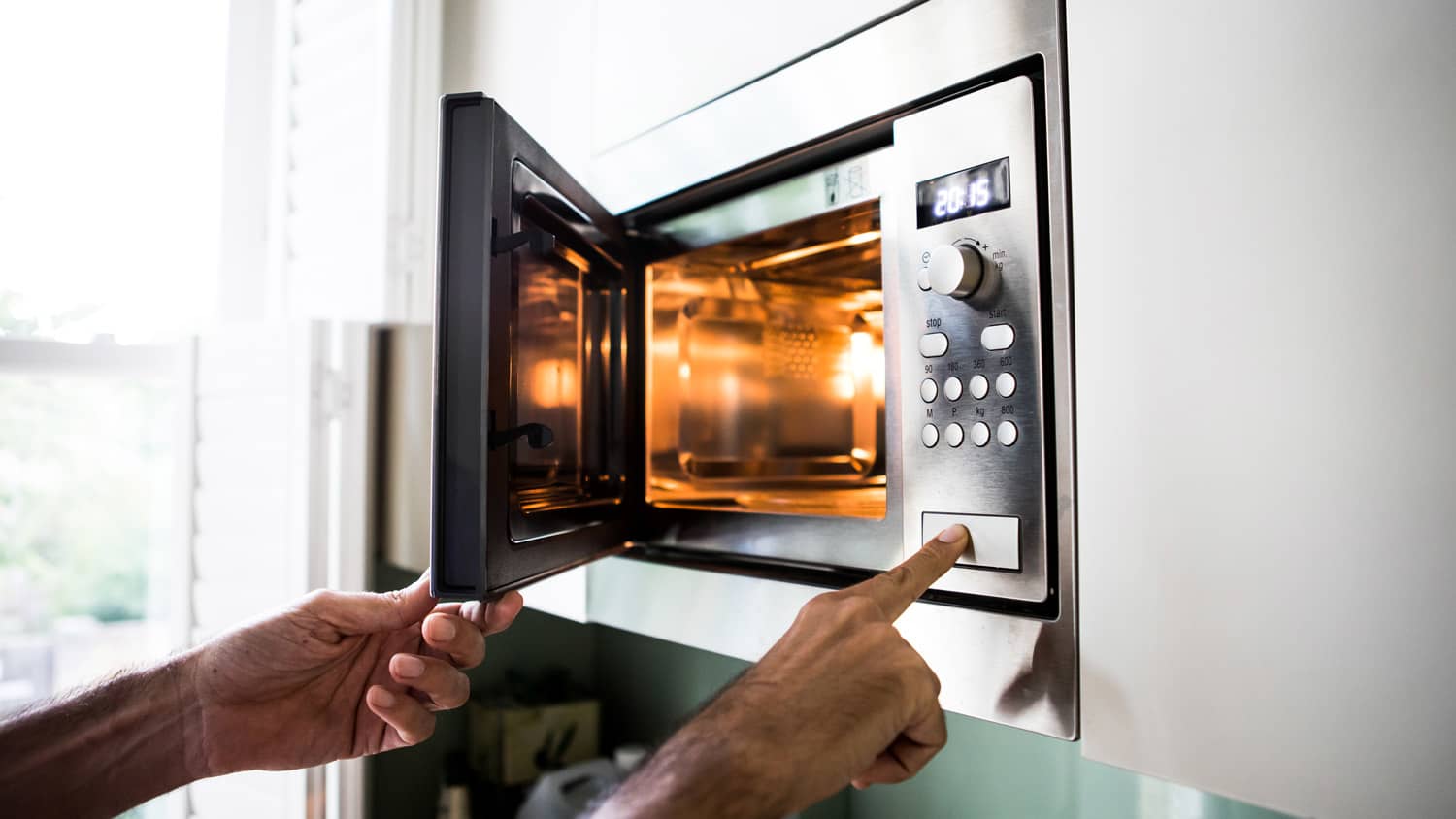 A man’s hand reheating food in the microwave
