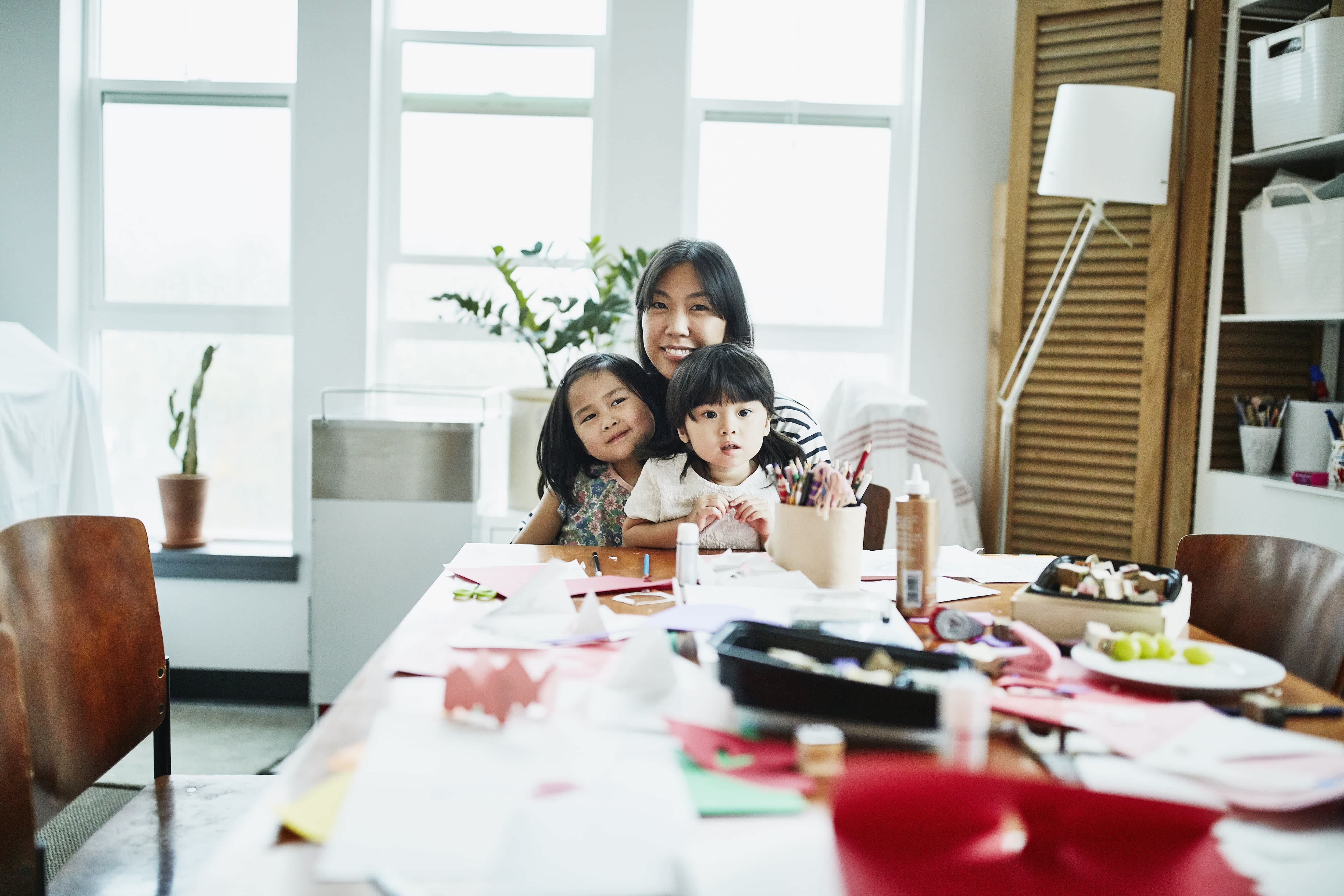 Mother and two small daughters sitting at table in craft room