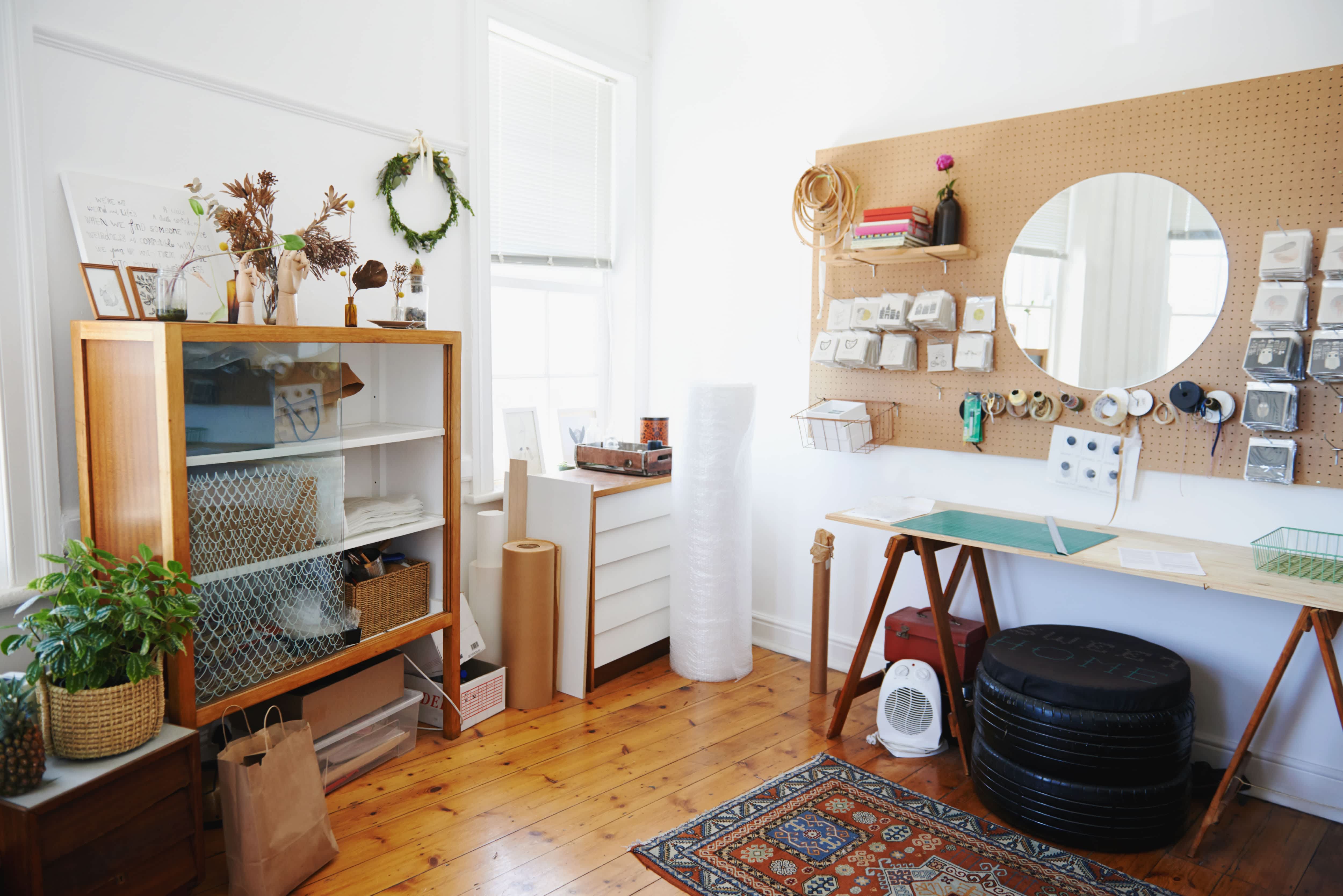 Craft room with vintage storage cabinets, wood floors, a rug, a workspace, and a pegboard wall
