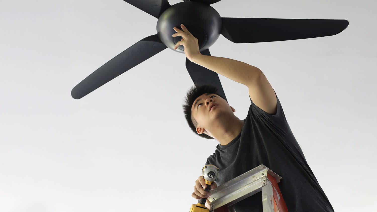 A young man adjusting a ceiling fan
