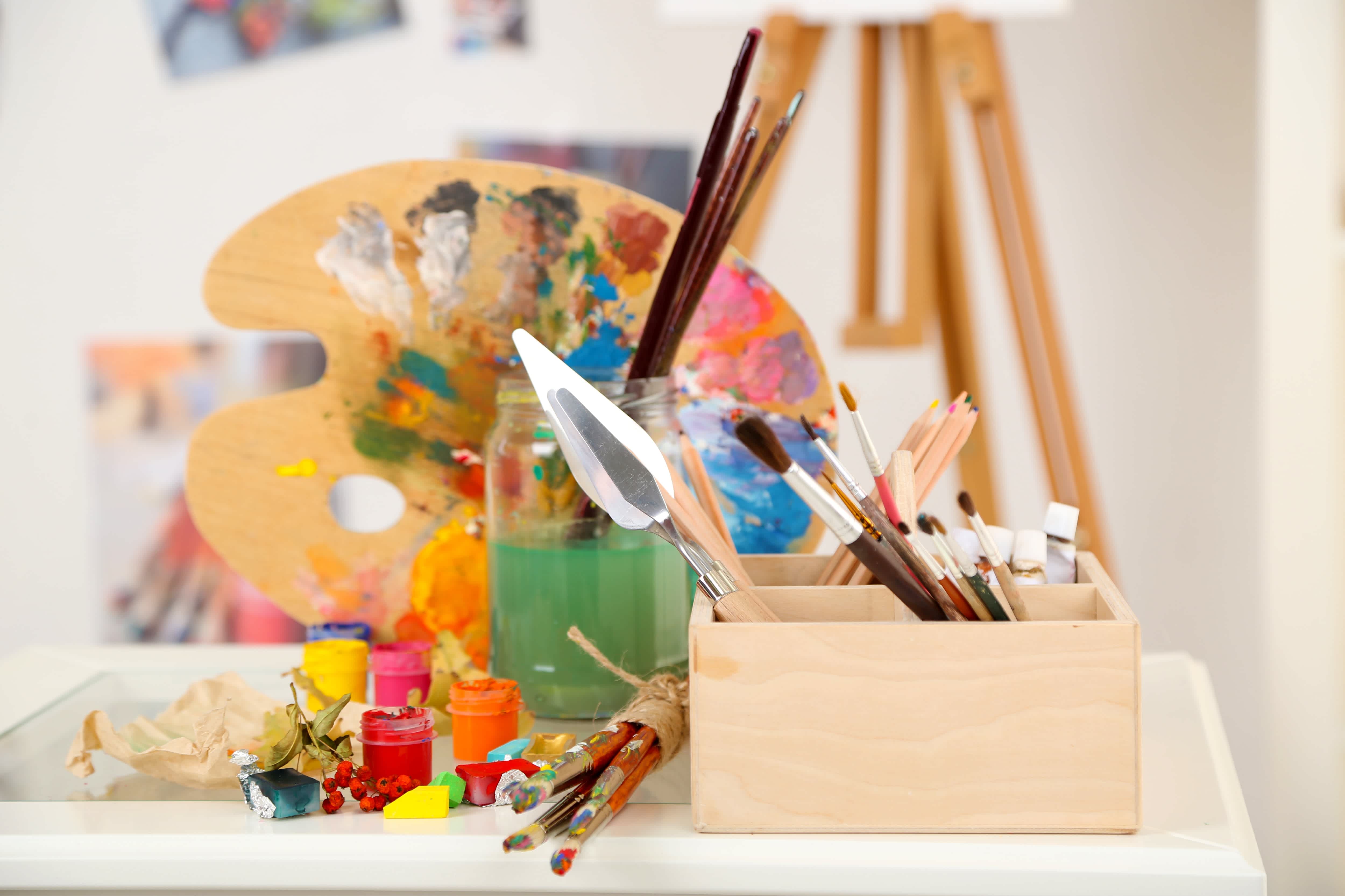 Toolbox on tabletop with paint brushes, glass jar, and paint supplies
