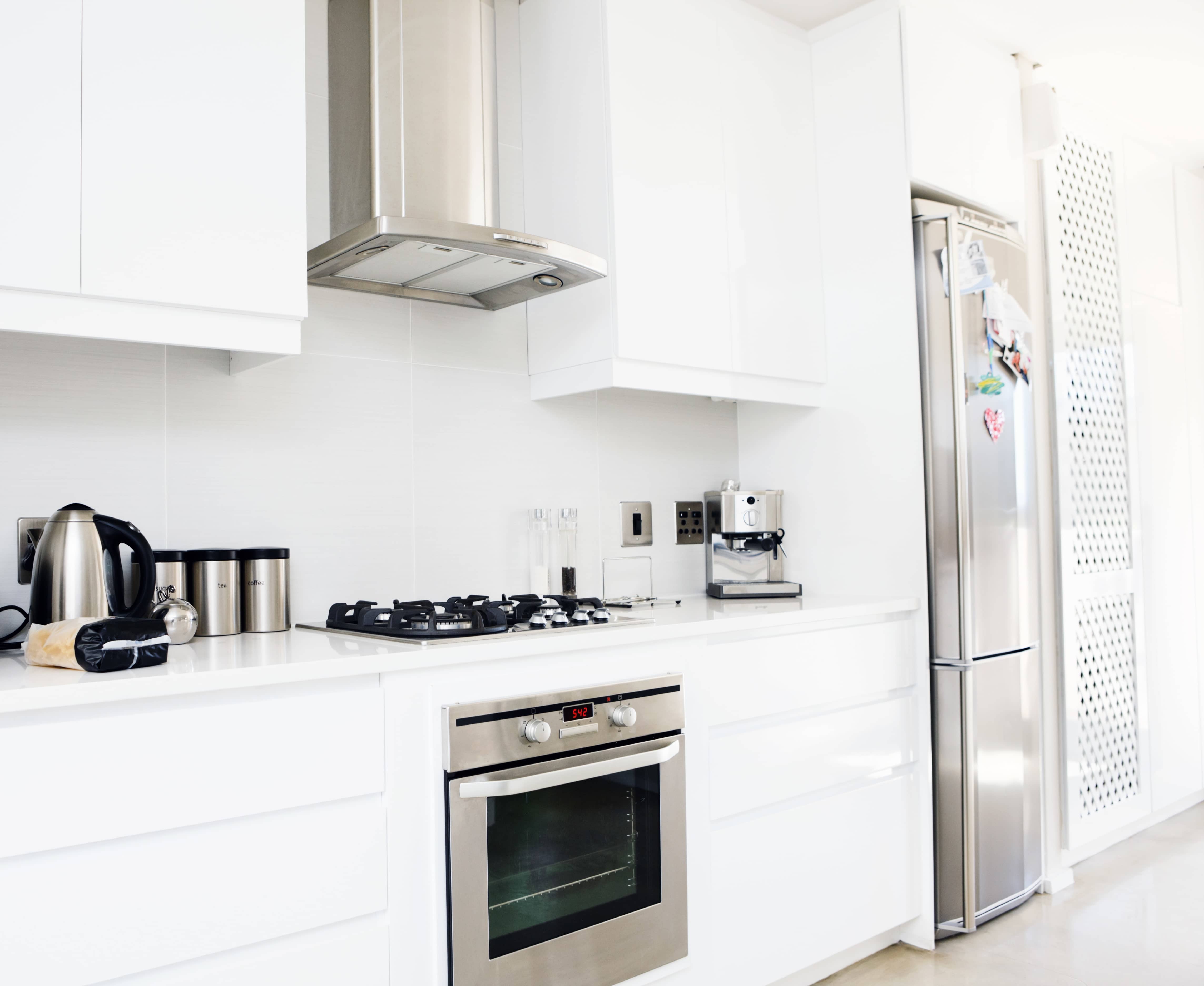 A white kitchen with stainless steel fridge, stove, range hood, and appliances