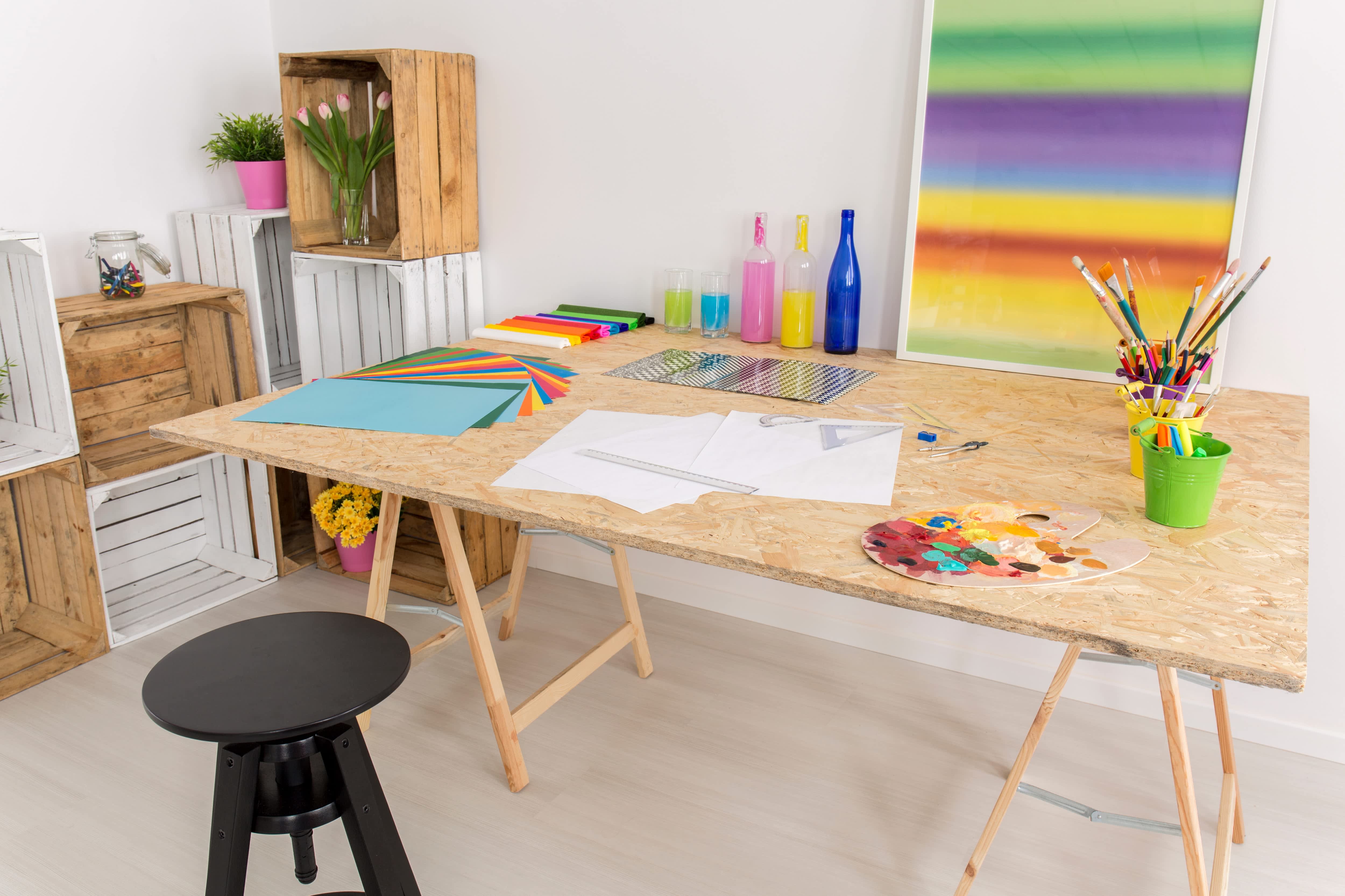 Craft room with plywood table, painting supplies, stool, and cube shelves made of storage bins