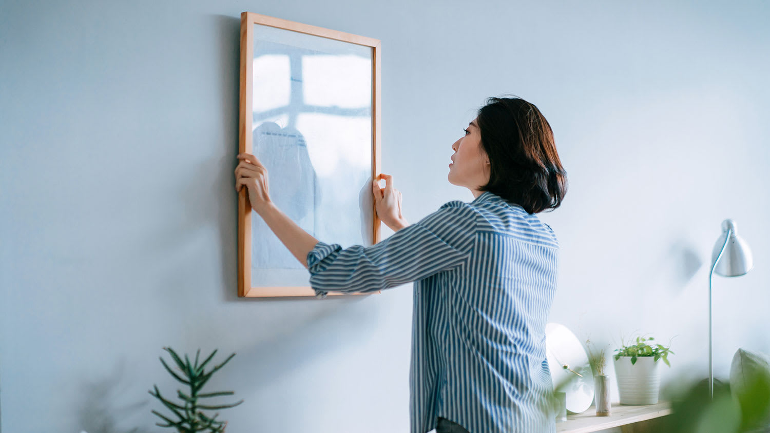 Woman in her apartment hanging picture frame on the wall