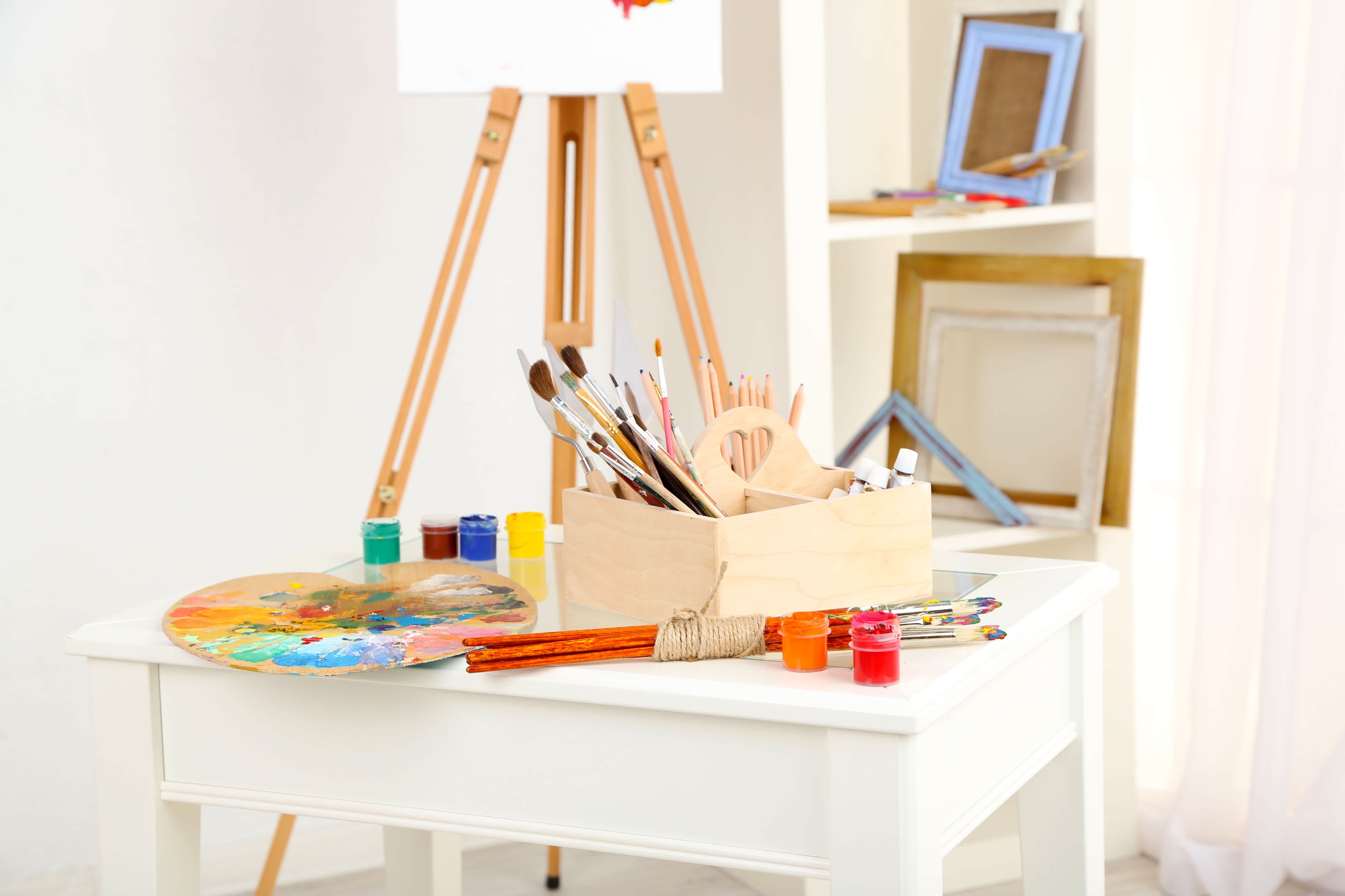 Craft room with island table, paint supplies, window, shelf, and easel