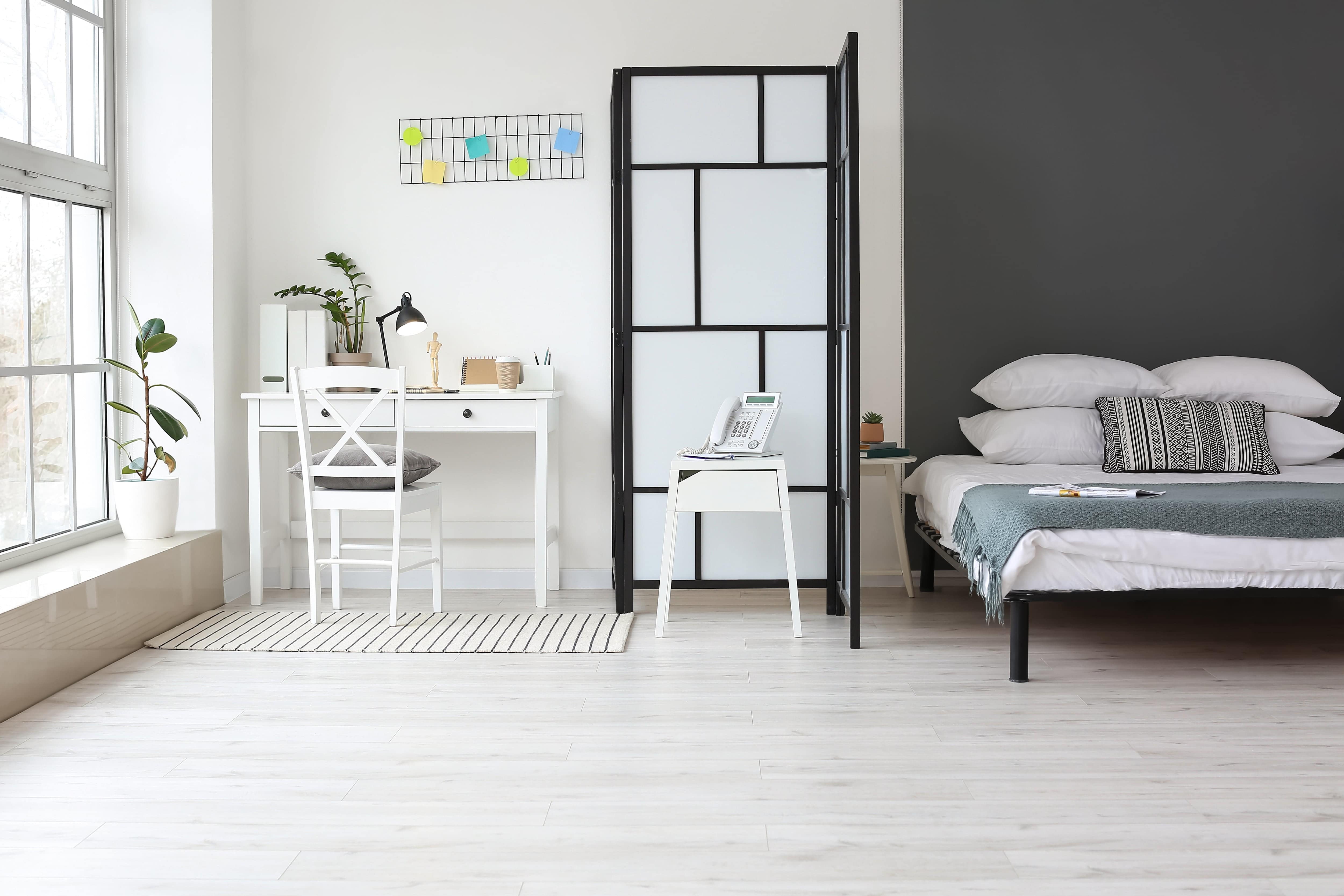 Modern bedroom with minimalist bed, a black and white room divider, and a stylish desk and chair