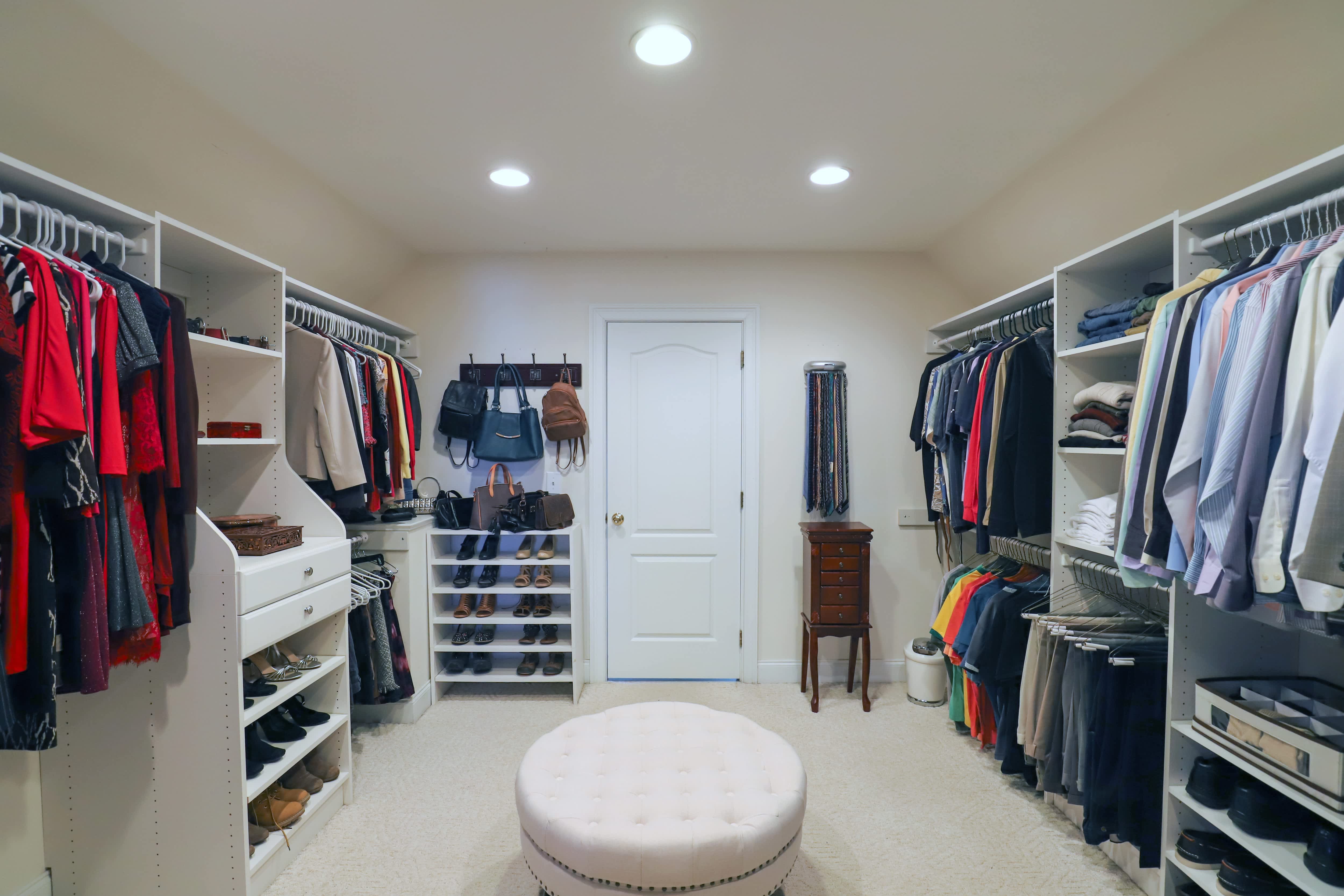 A his and hers walk-in closet with a fabric covered stool