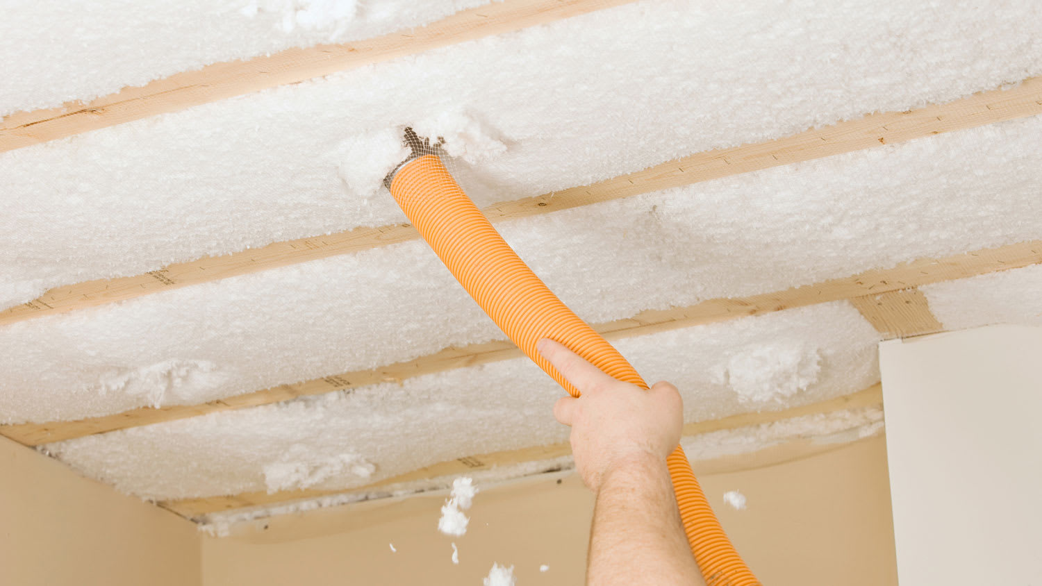 Worker blowing insulation between floor joists