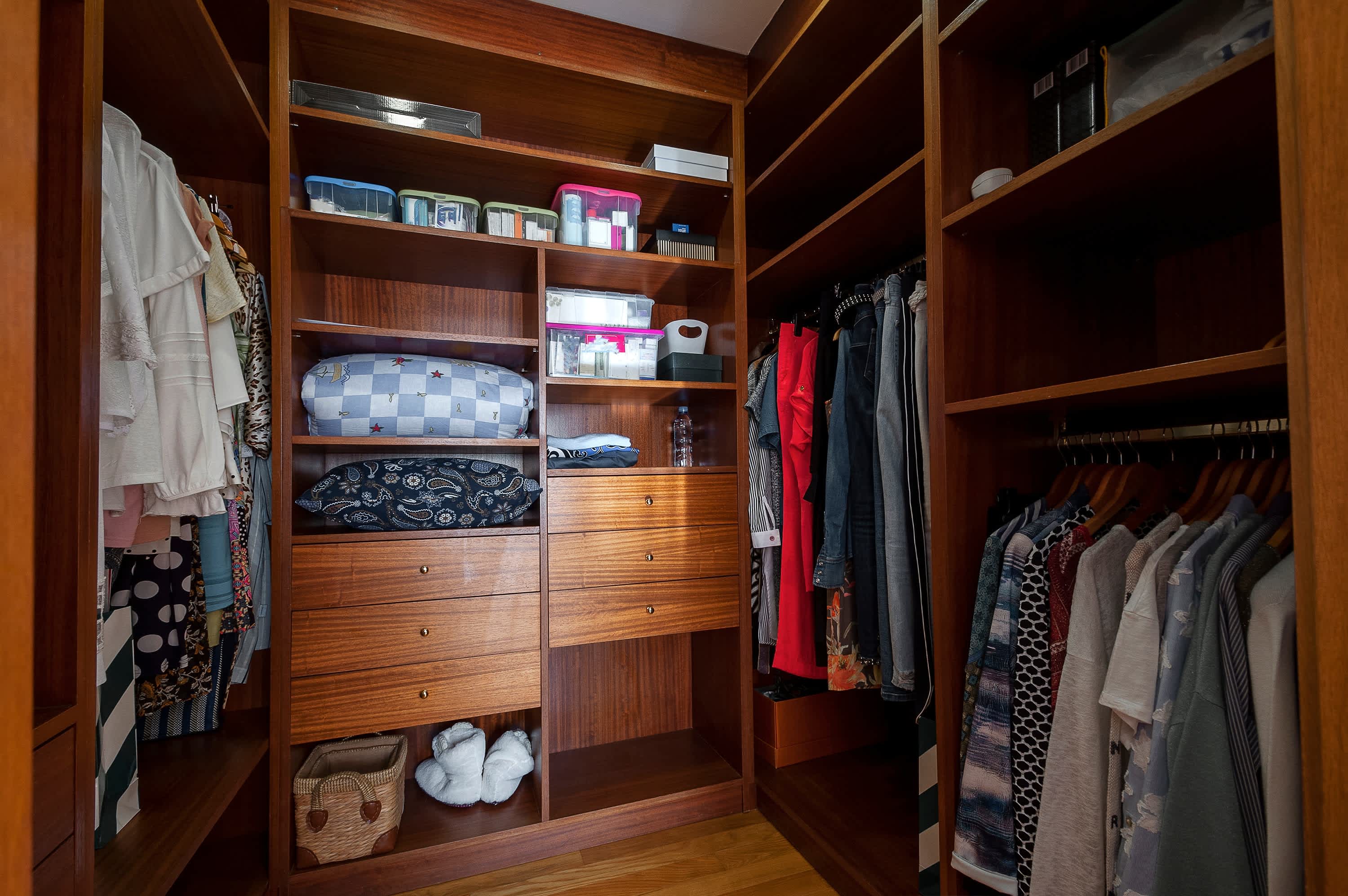 A small walk-in closet with dark wood shelves and drawers