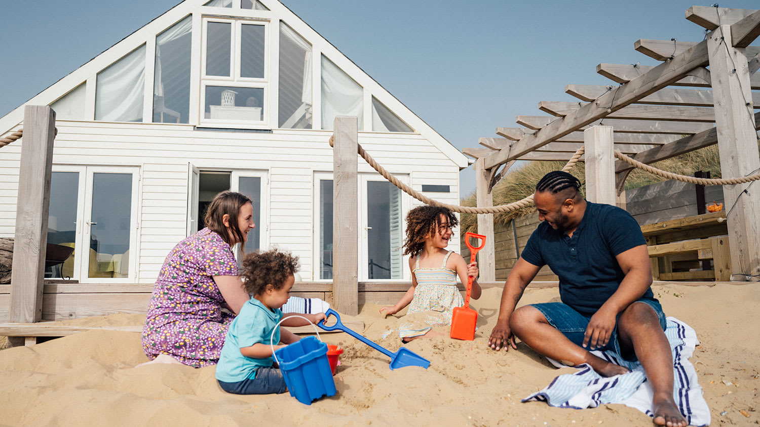 family sitting on the beach in front of house