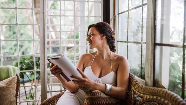 Woman reading book in sunroom and smiling