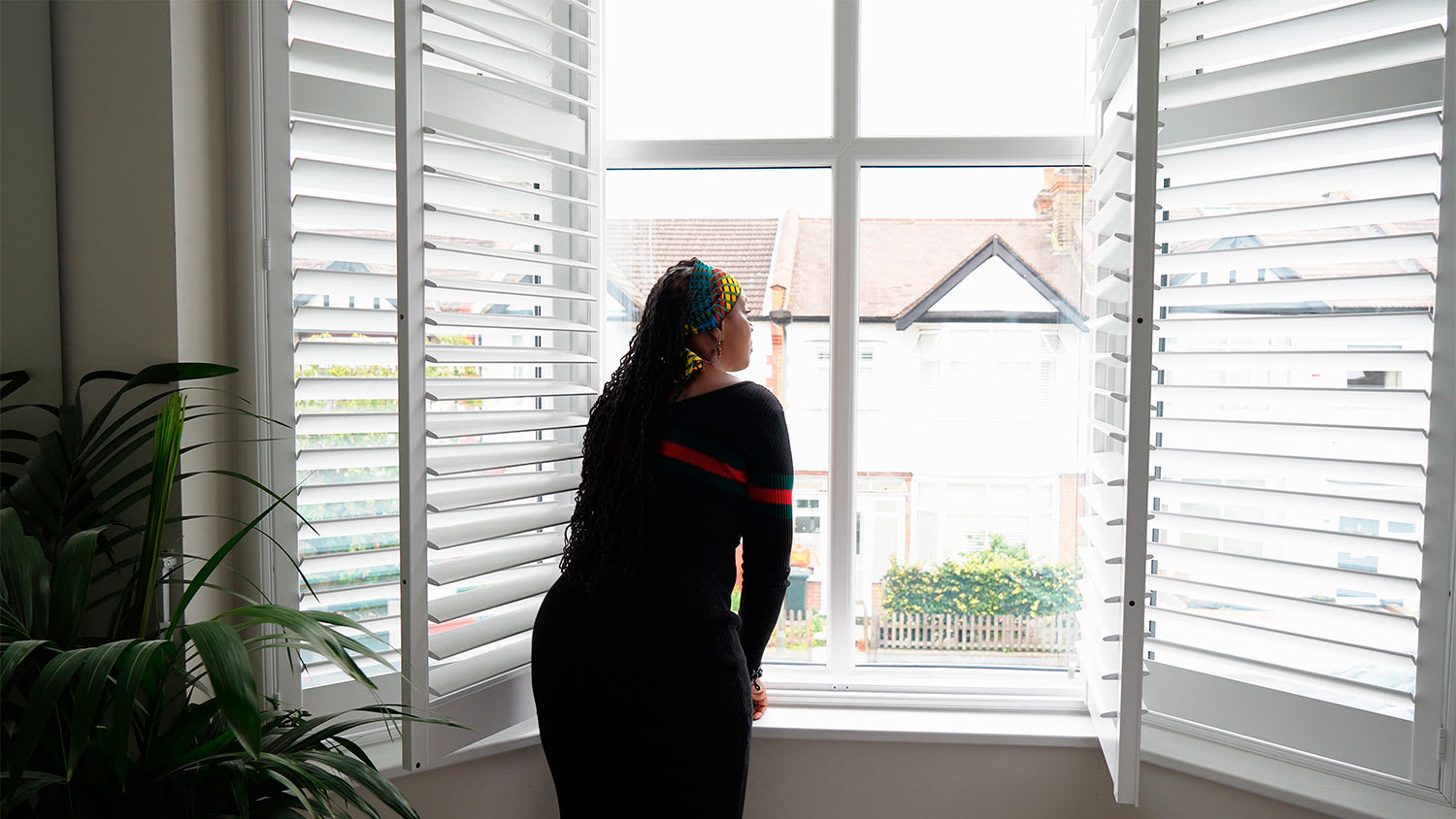 A woman stands at a window with shutters