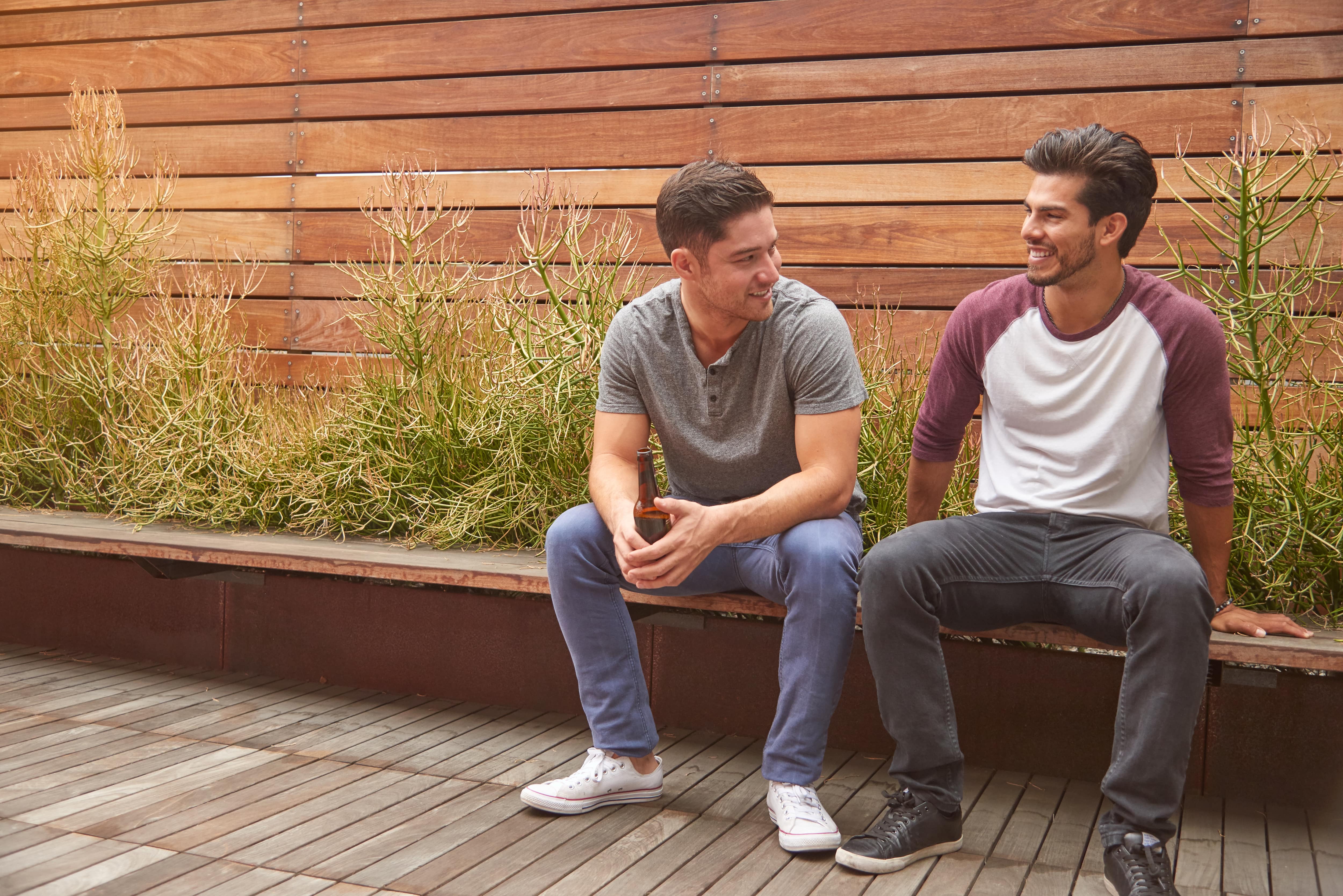 Two men sitting in front of modern fence with horizontal slats