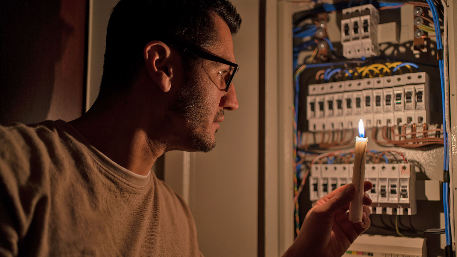 man checking fuse box with a candle after power outage