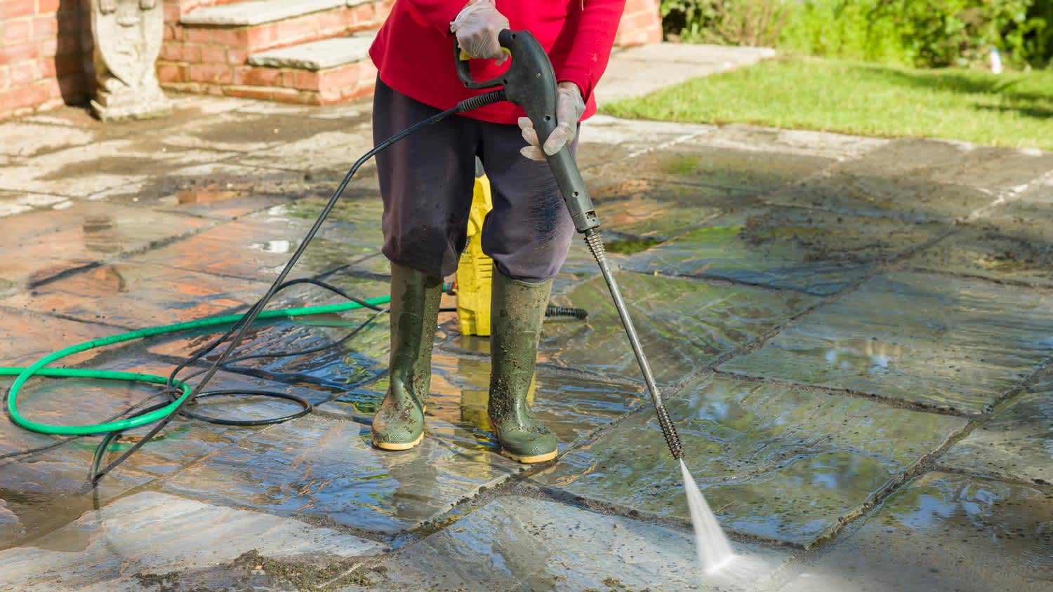 A person pressure washing a patio of a house