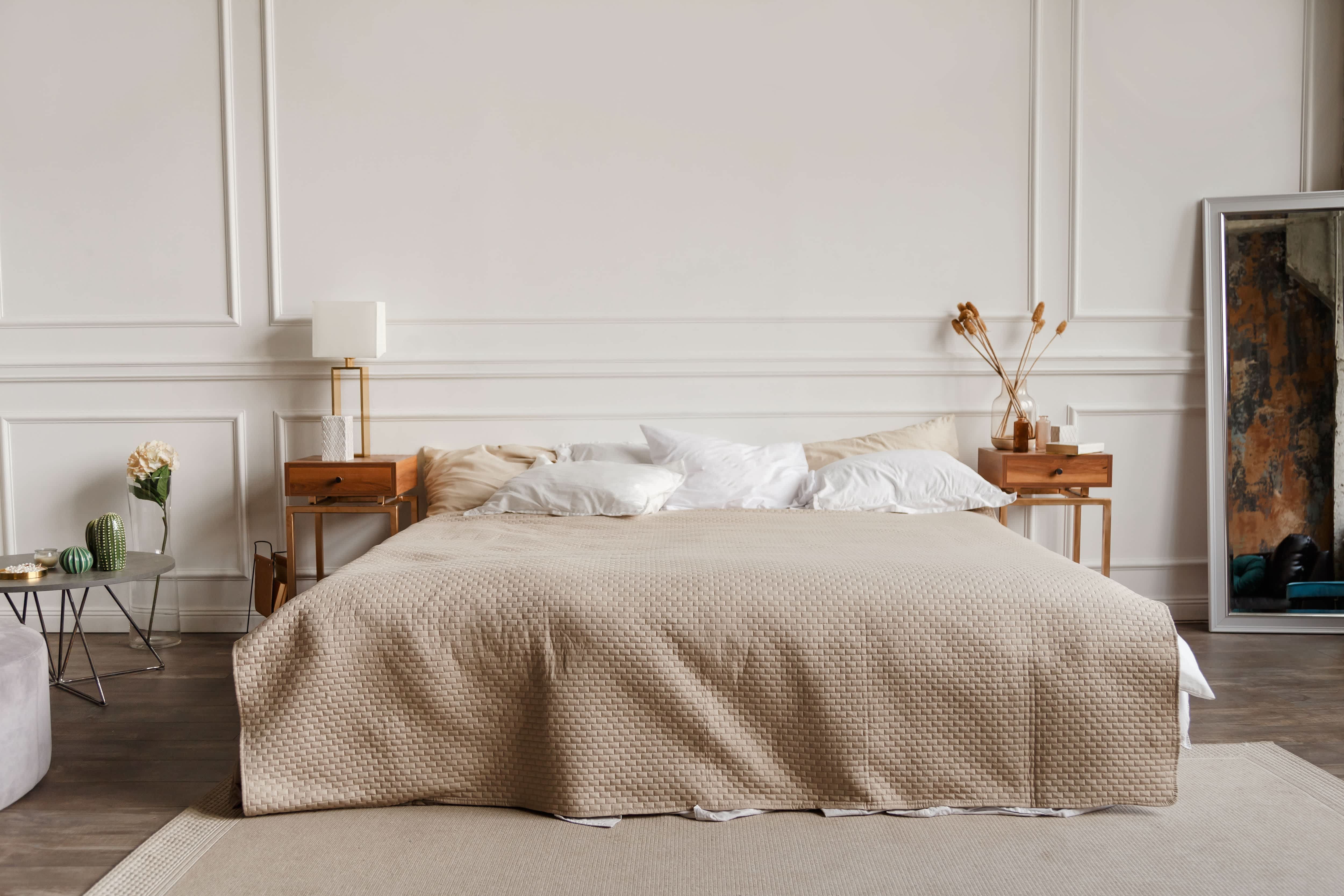 Luxury bedroom with tan bedding and rug, small modern end tables, and wainscoting wall paneling