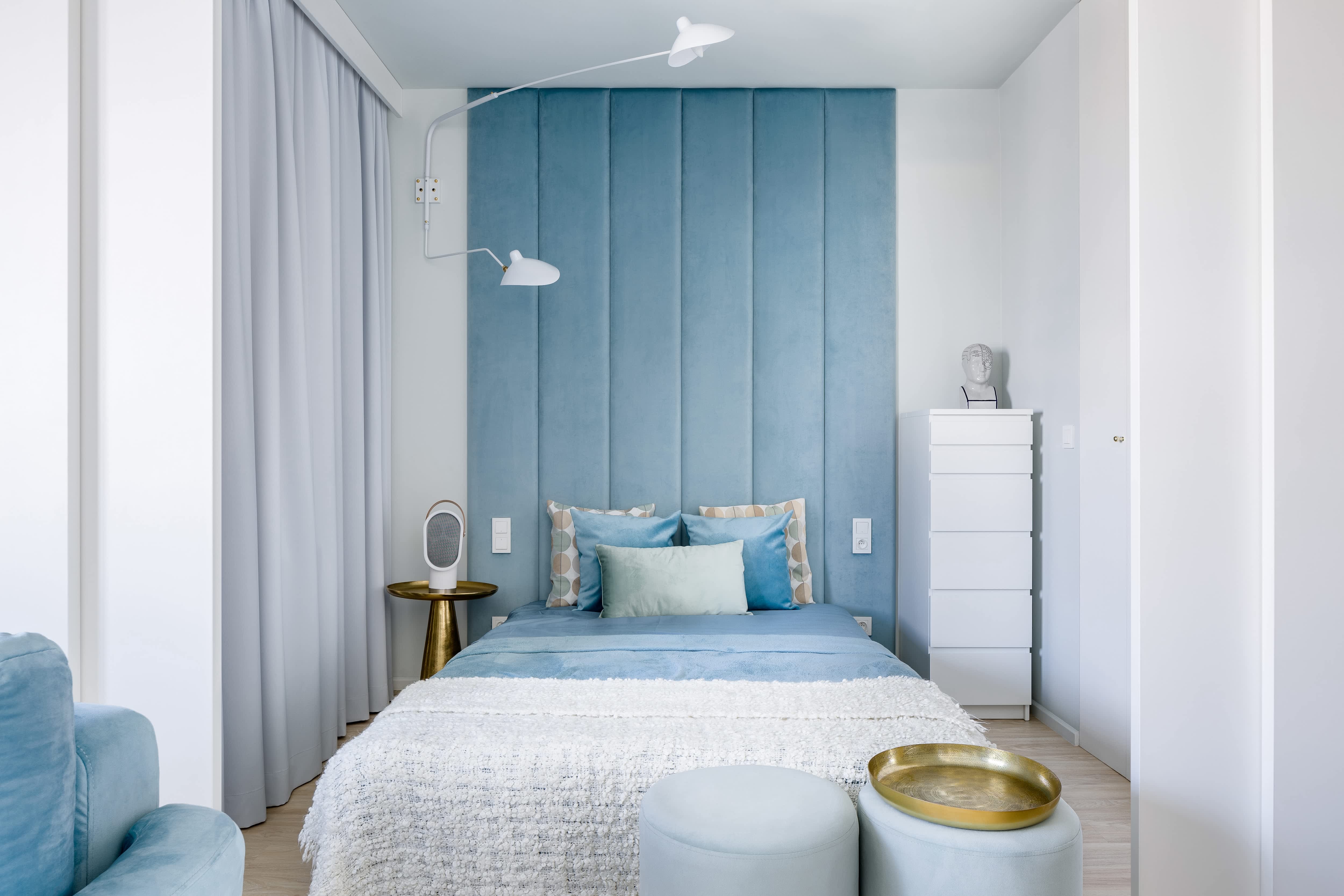 Small, narrow white bedroom with upholstered fabric wall panel behind bed